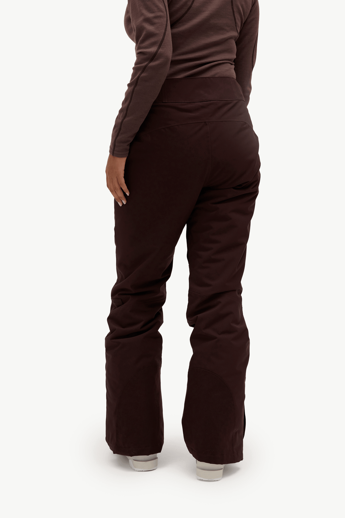 Rear view of a person wearing dark brown pants and a matching dark brown long-sleeve top against a clean white studio background.