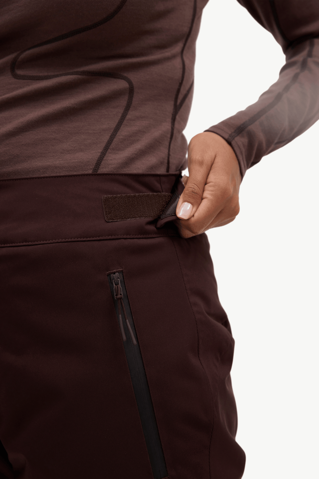 Close-up of a person wearing dark brown athletic pants and a matching long-sleeve top, pulling a side pocket flap to show the interior.