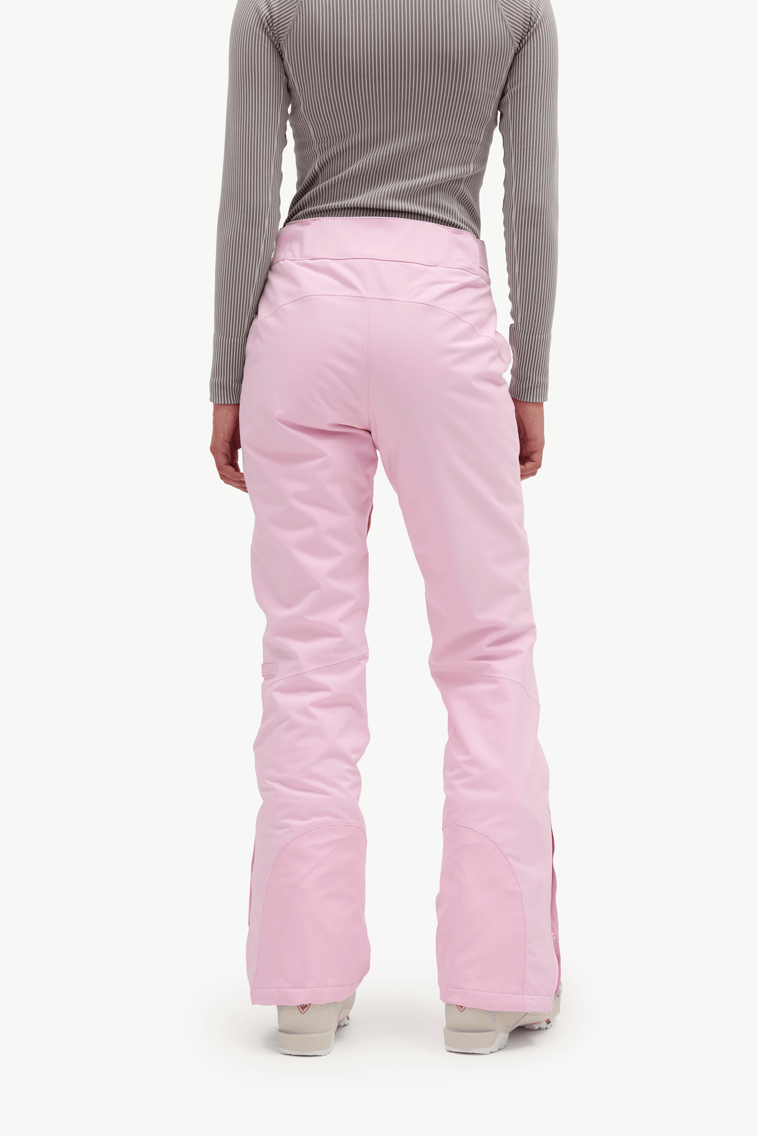 A person shown from the back wearing light pink ski pants, a gray ribbed long-sleeve top, and light-colored shoes against a plain white studio background.