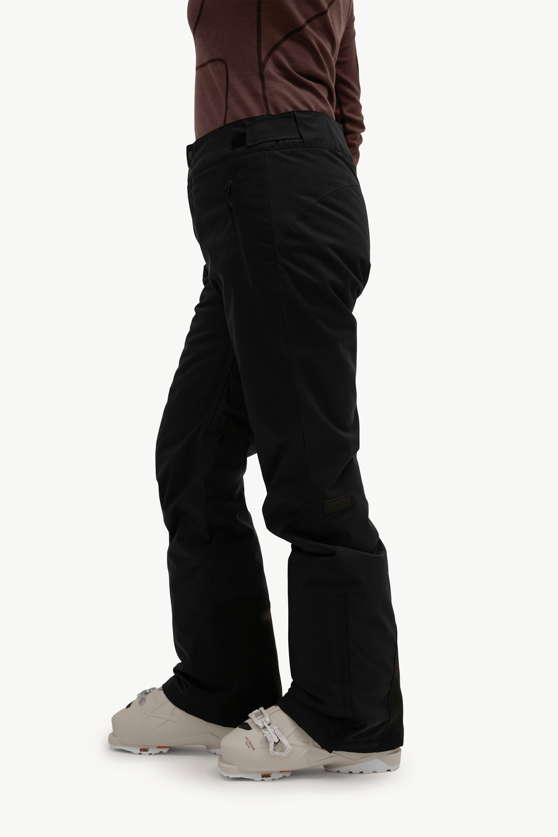 A person shown from the waist down wearing black snow pants, a brown top, and off-white snow boots against a plain light background.