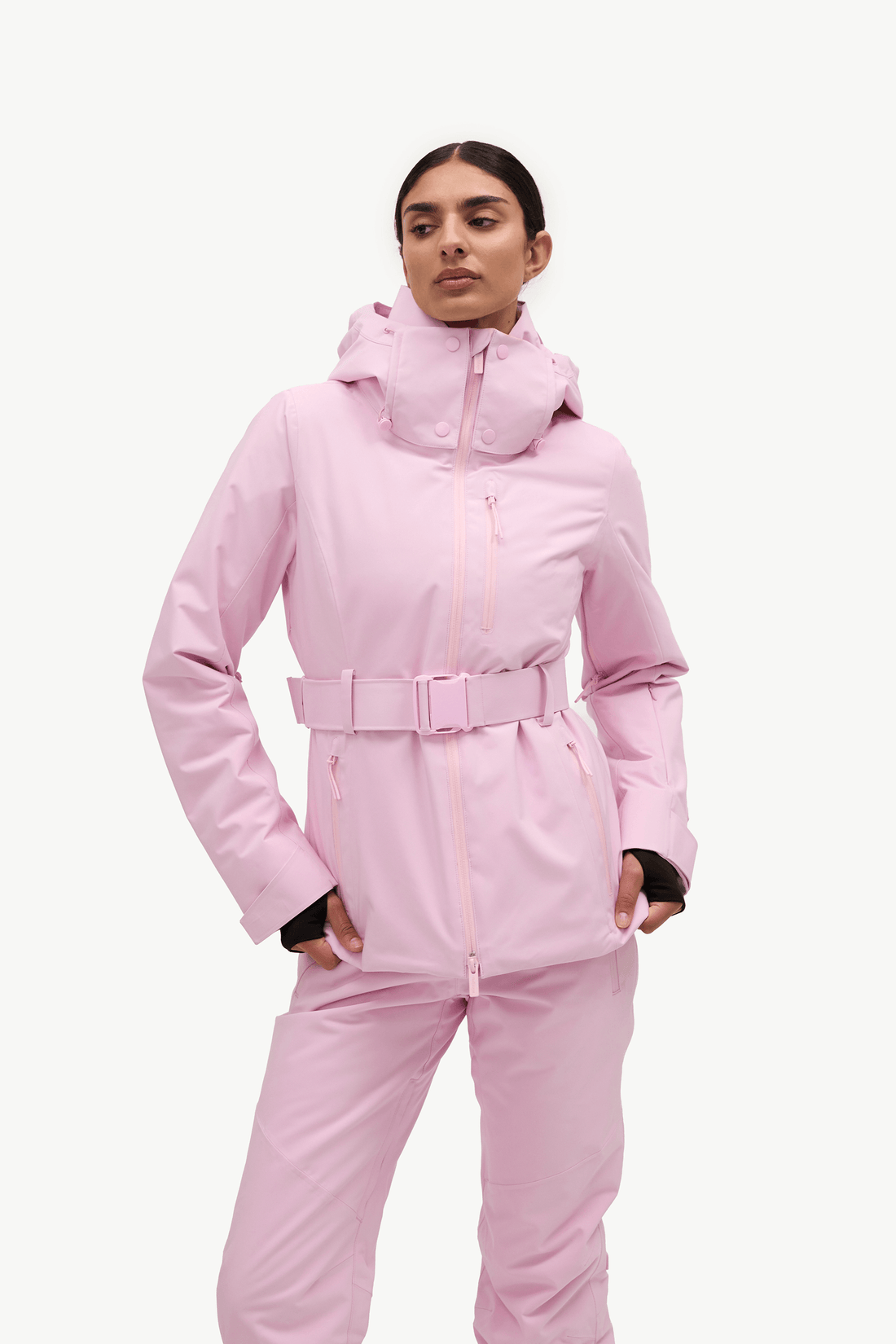 A woman modeling a light pink ski jacket and matching pants against a plain white studio background.