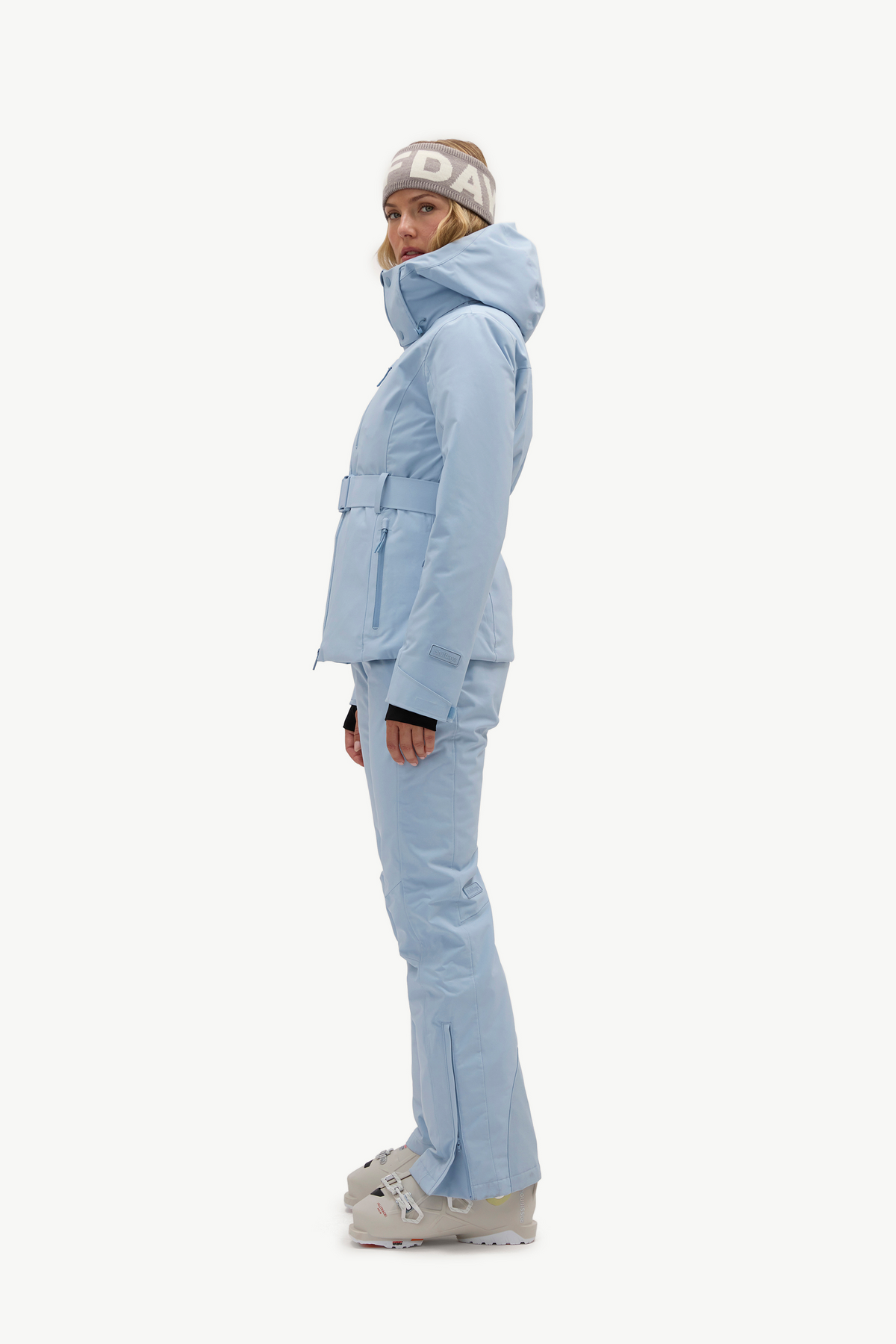 A woman modeling a light blue ski jacket and matching ski pants, against a plain white studio background.