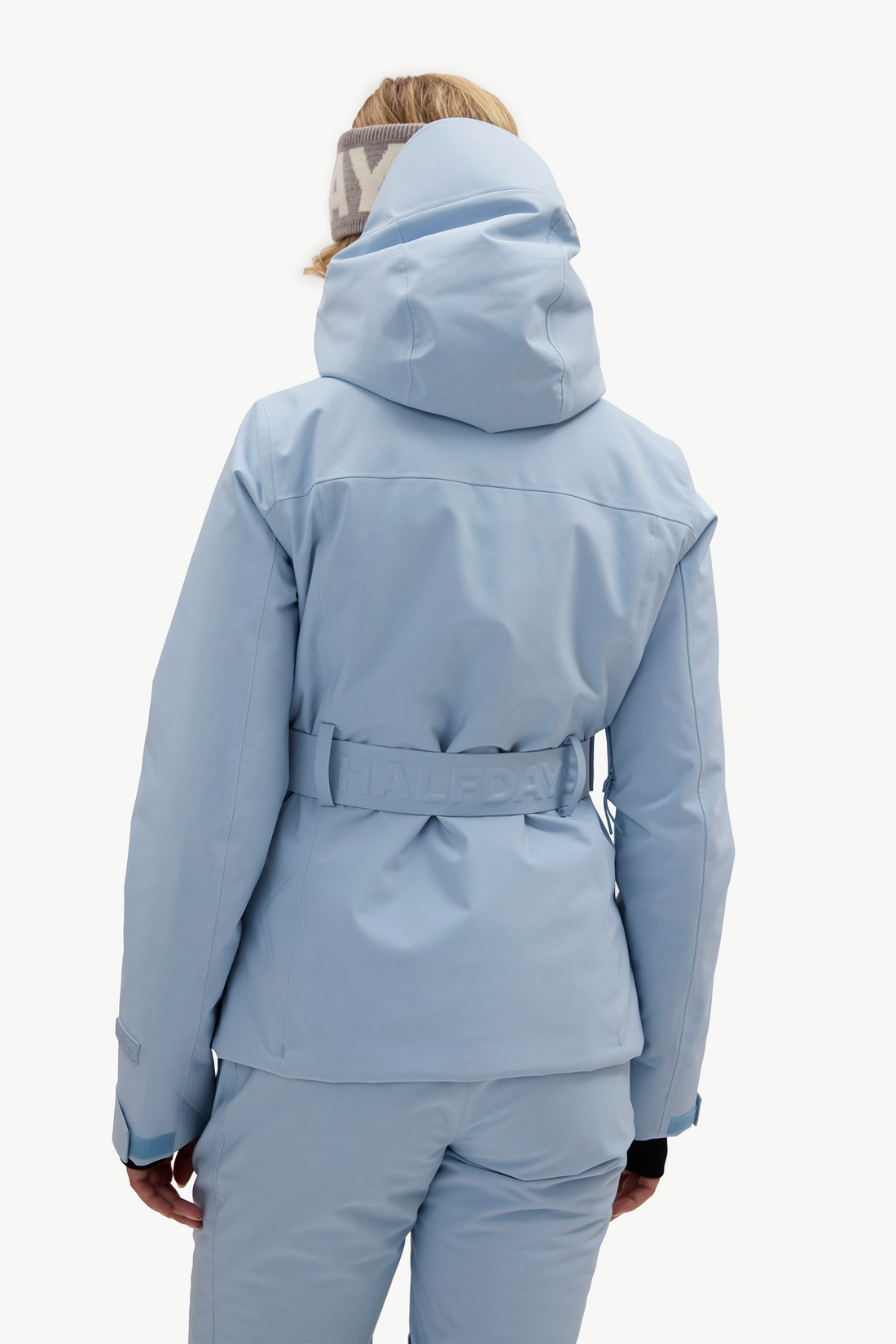 A woman modeling a light blue ski jacket and matching ski pants, against a plain white studio background.