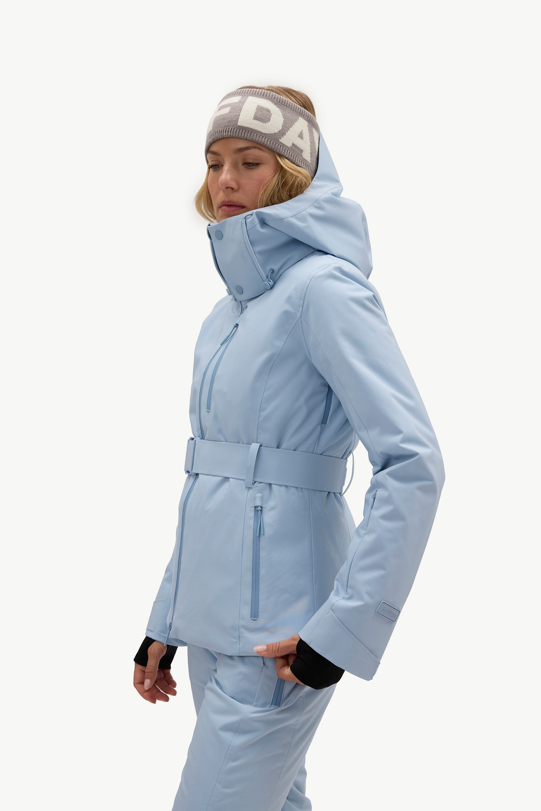 A woman modeling a light blue ski jacket and matching ski pants, against a plain white studio background.