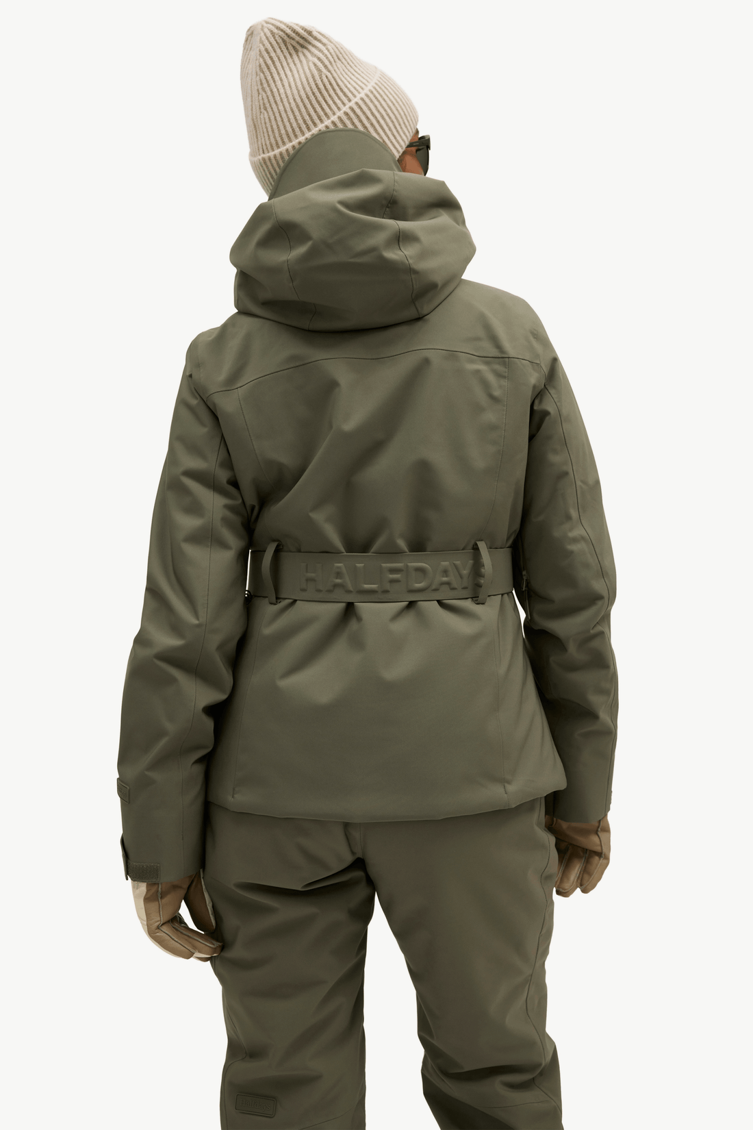 A model shown from the back wearing a Halfda ski jacket in olive green, matching pants, gloves, and a beige knit beanie against a plain white background.