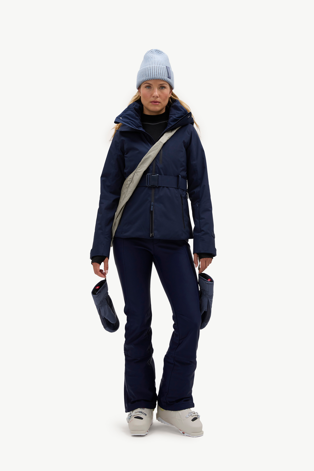 A woman wearing a dark navy hooded jacket, matching navy pants, and light gray ski boots, standing against a plain white studio background.