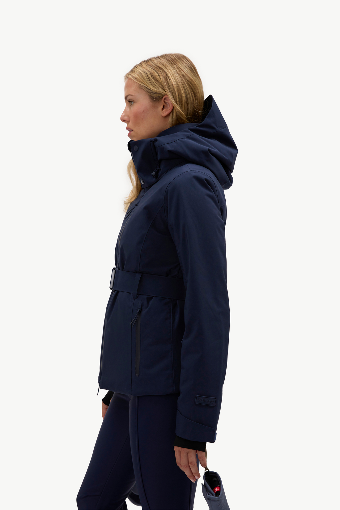 A woman wearing a dark navy hooded jacket, matching navy pants, and light gray ski boots, standing against a plain white studio background.