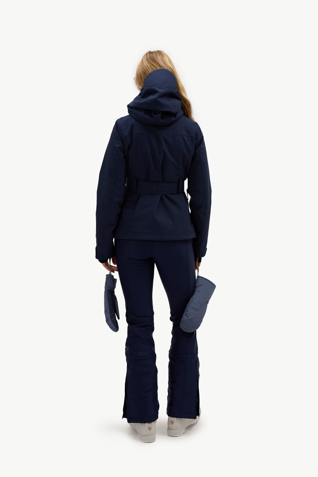 A woman wearing a dark navy hooded jacket, matching navy pants, and light gray ski boots, standing against a plain white studio background.
