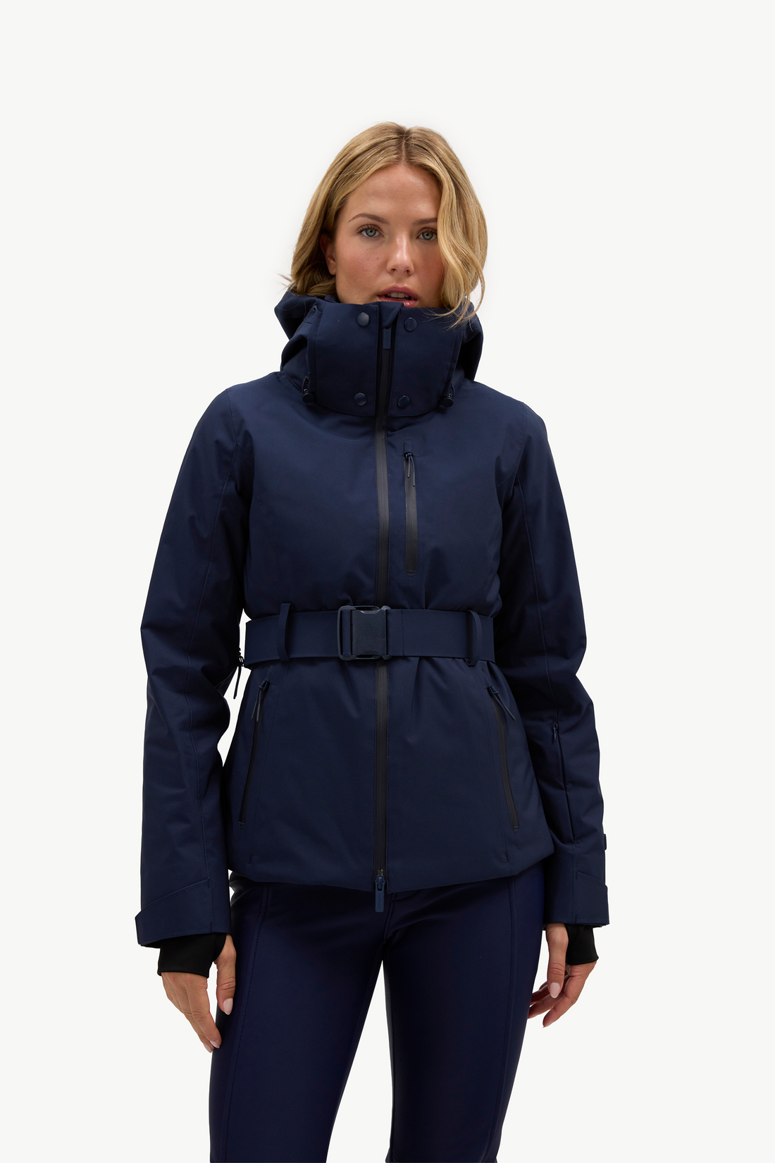 A woman wearing a dark navy hooded jacket, matching navy pants, and light gray ski boots, standing against a plain white studio background.