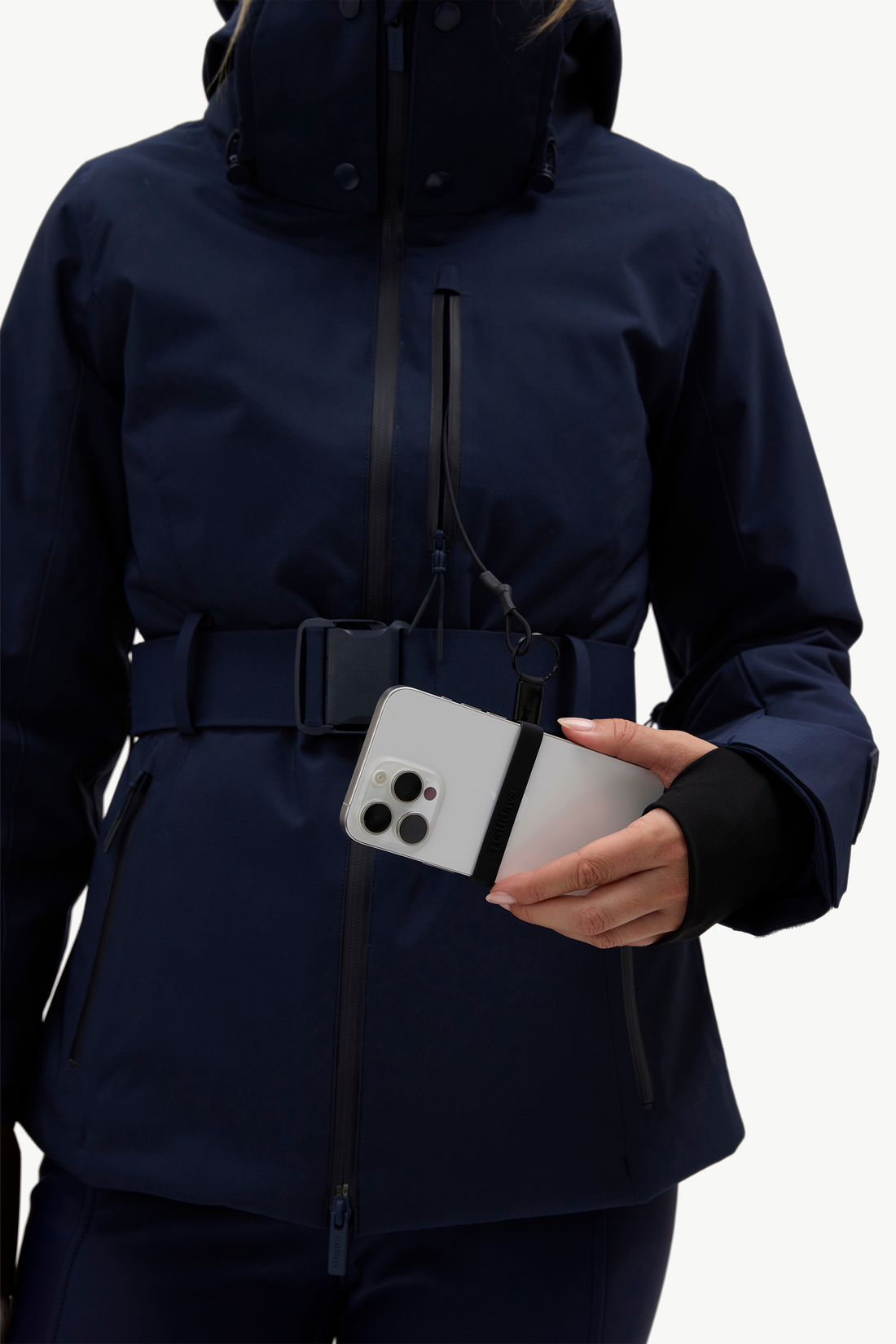 A woman wearing a dark navy hooded jacket, matching navy pants, holding a phone standing against a plain white studio background.