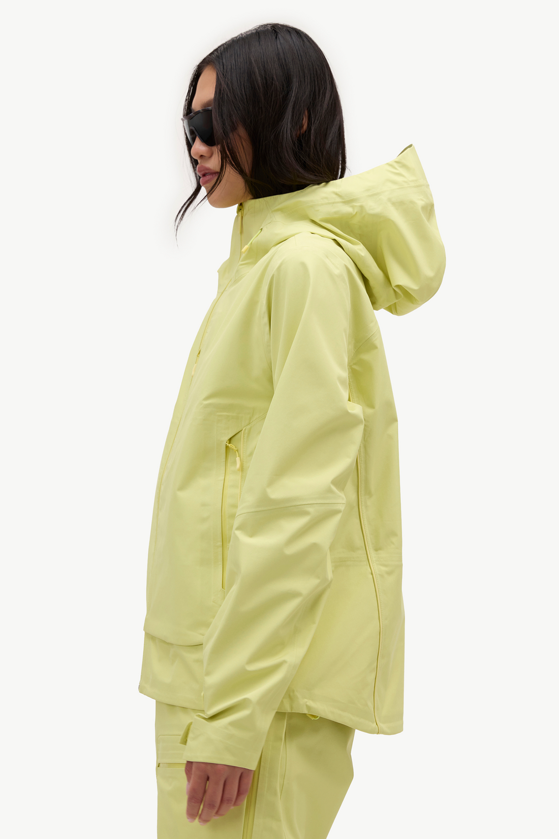 A model in side profile wearing a light yellow hooded jacket and matching pants against a plain white studio background.