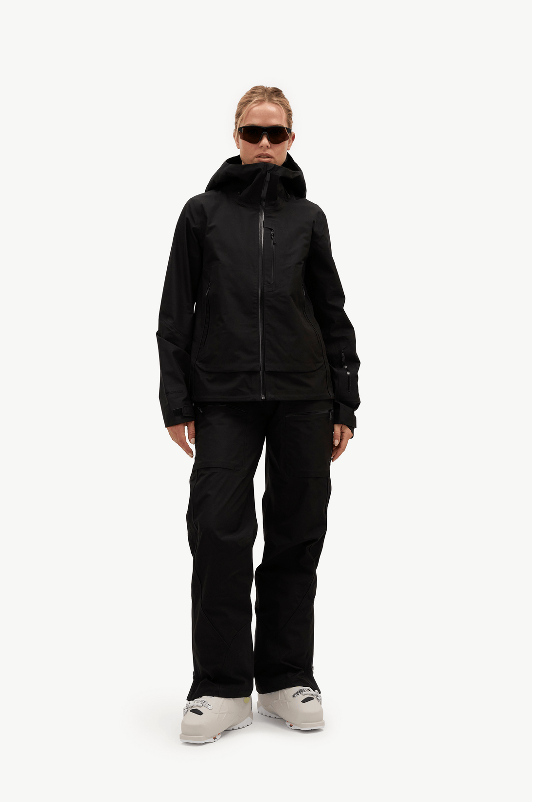 A model wearing a black ski jacket, black ski pants, and light gray snowboard boots, standing against a solid white studio background.