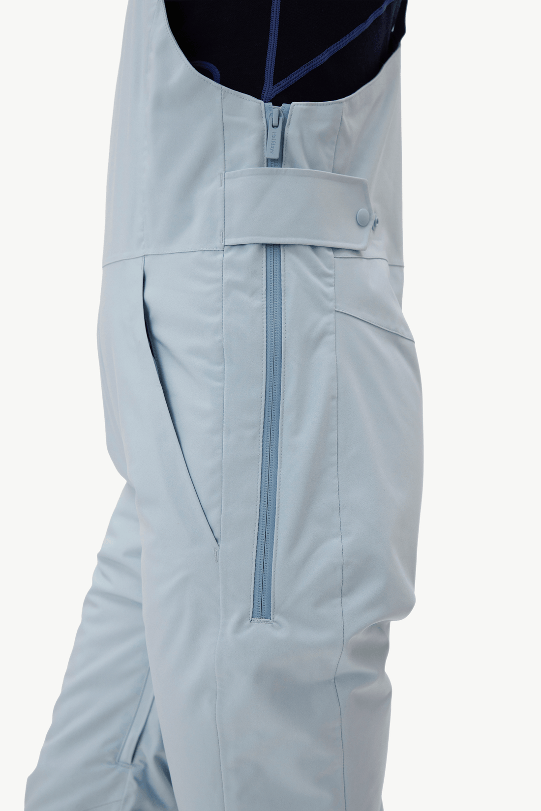 Close-up of light blue snow pants with a central zipper and side pocket, worn over a dark top against a plain light background.