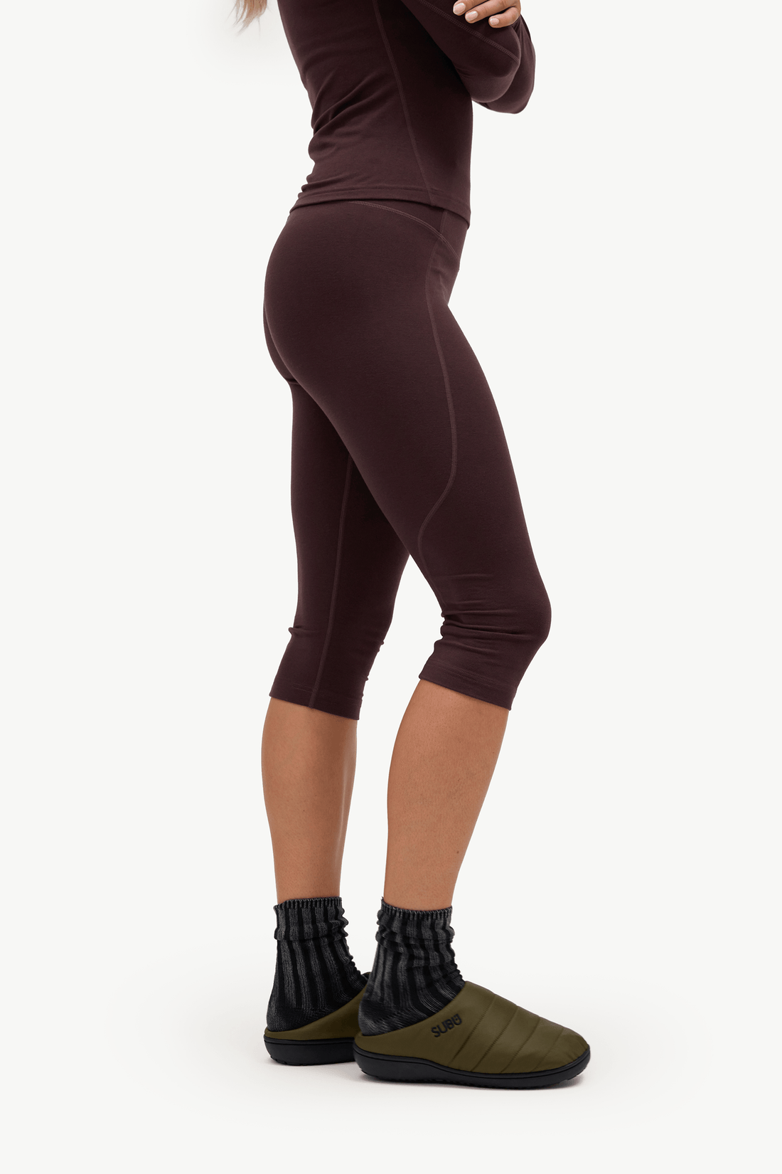 A model shown from the waist down wearing dark brown capri leggings, black ribbed socks, and olive green slip-on shoes against a plain white background.