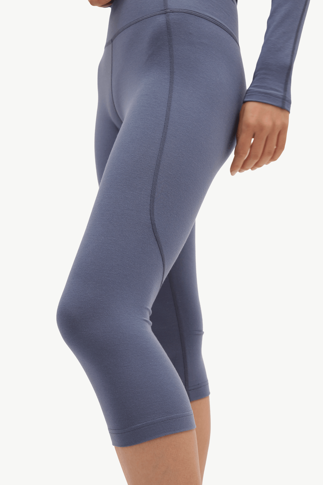 A close-up side view of a person wearing fitted capri leggings in a muted dusty blue-gray color against a plain light background.
