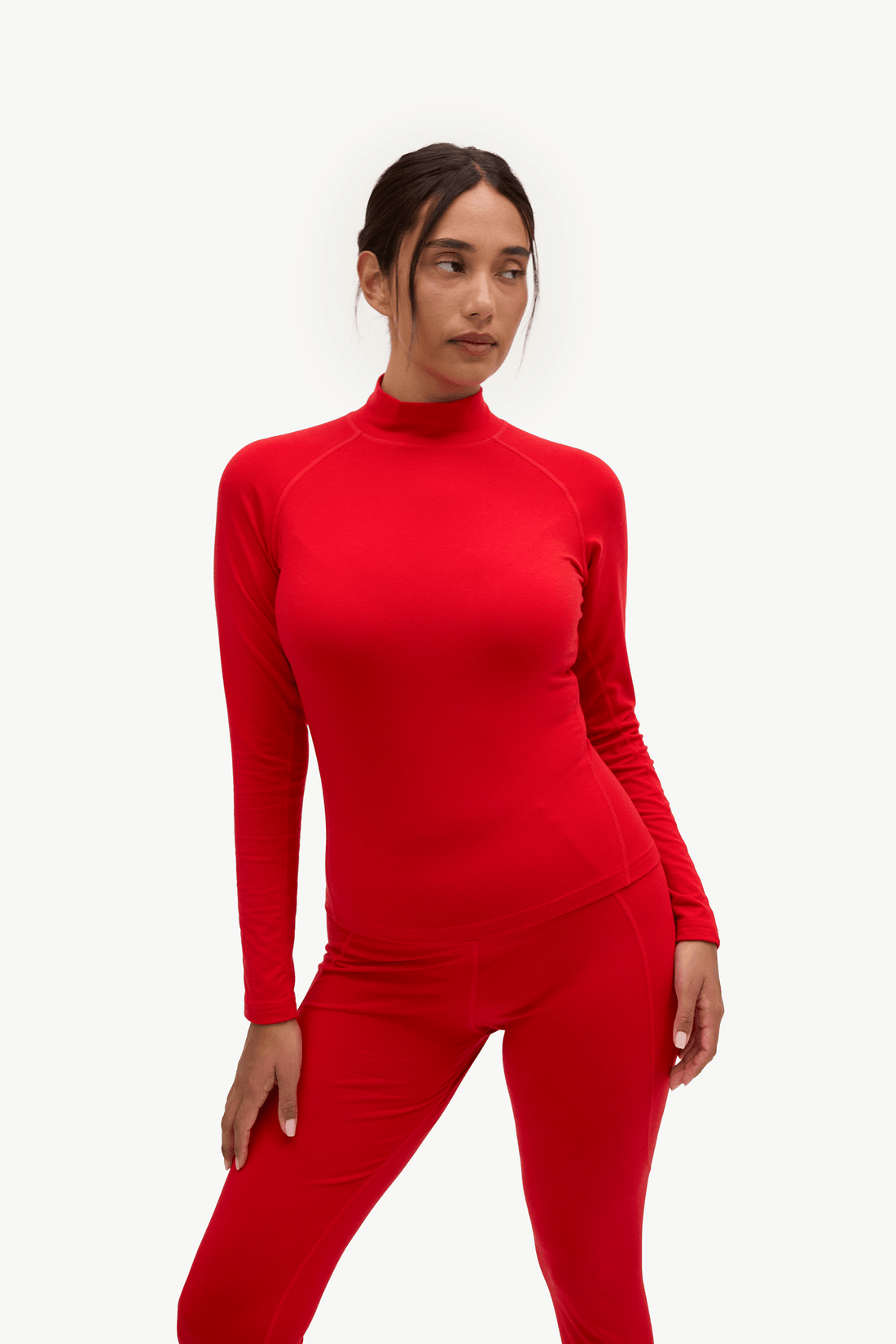 A woman modeling a bright red long-sleeve mock neck top and matching red leggings against a plain white studio background.