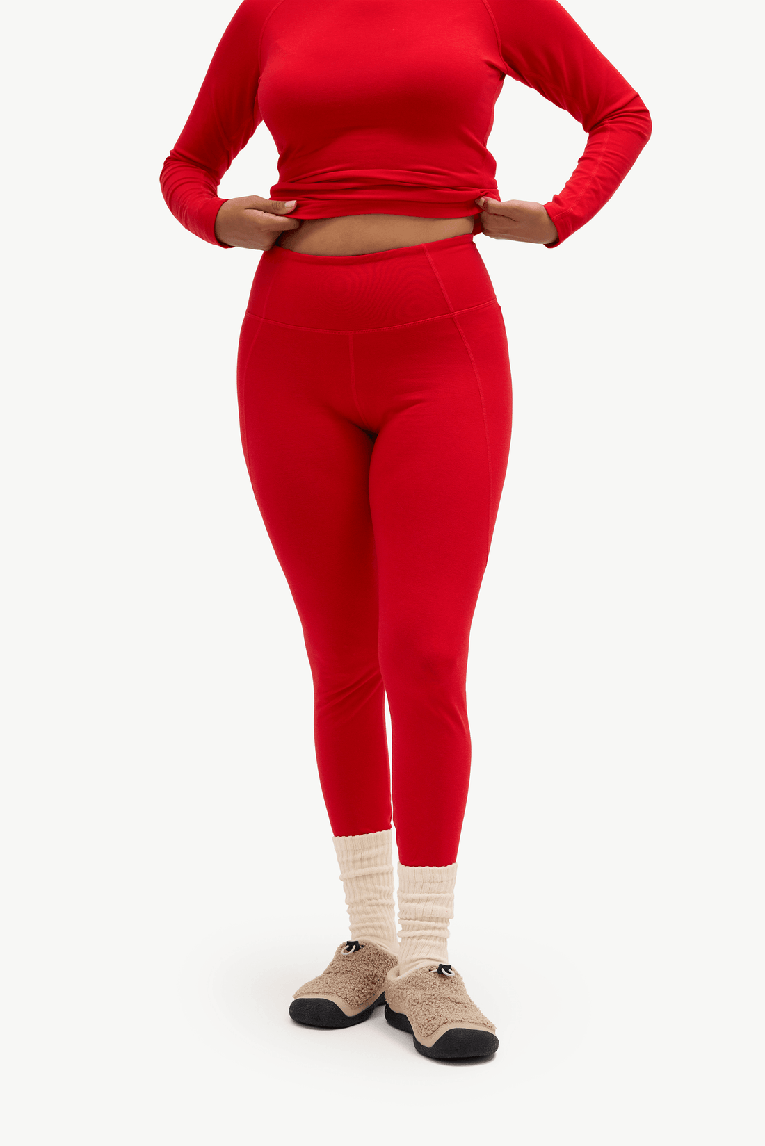 A model wearing a matching red long-sleeve crop top and high-waisted leggings, paired with cream ribbed socks and beige slip-on shoes, against a plain white background.