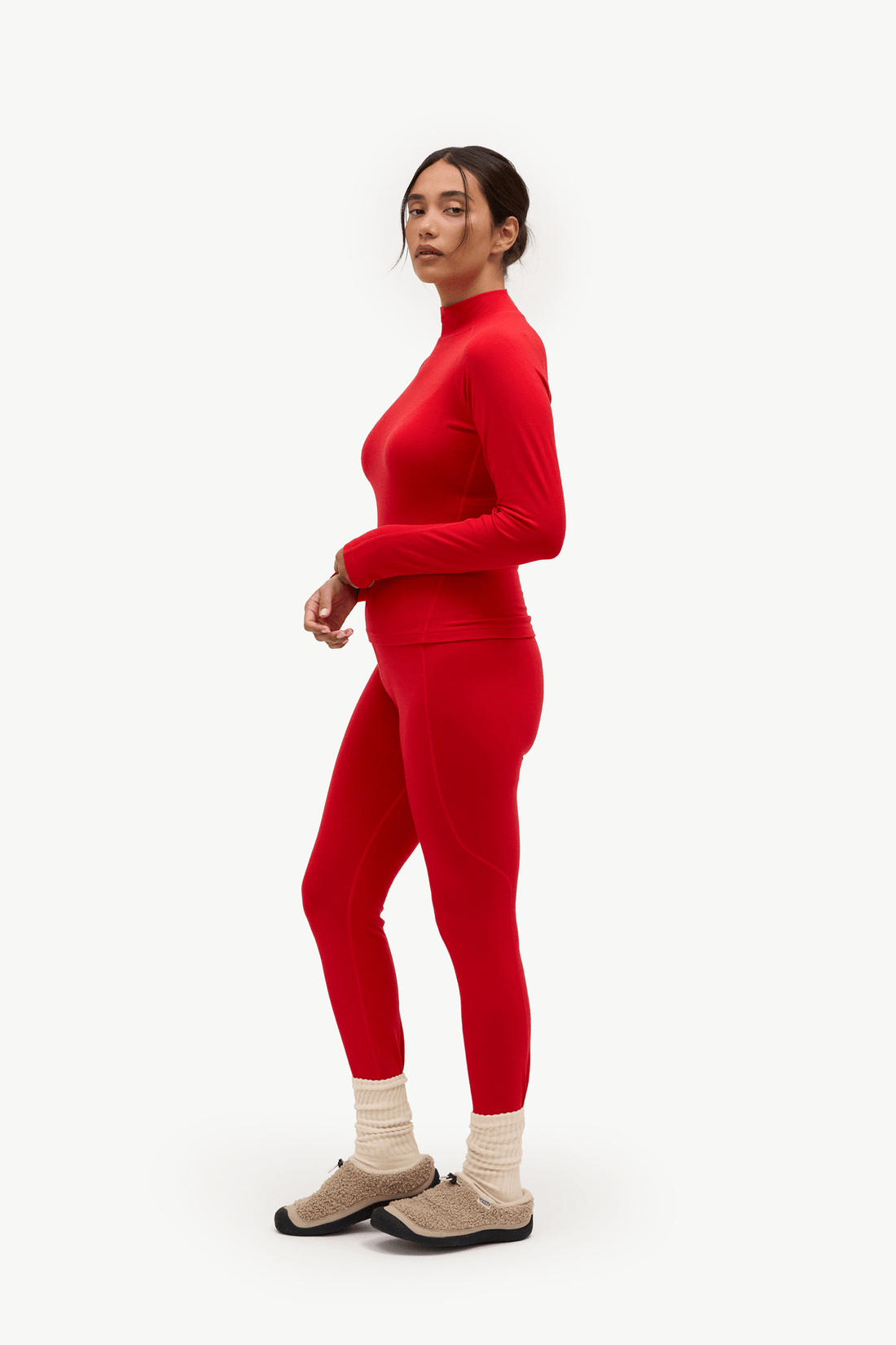 A woman modeling a matching red long-sleeve mock neck top and leggings set, paired with beige socks and brown slip-on shoes, against a plain white studio background.
