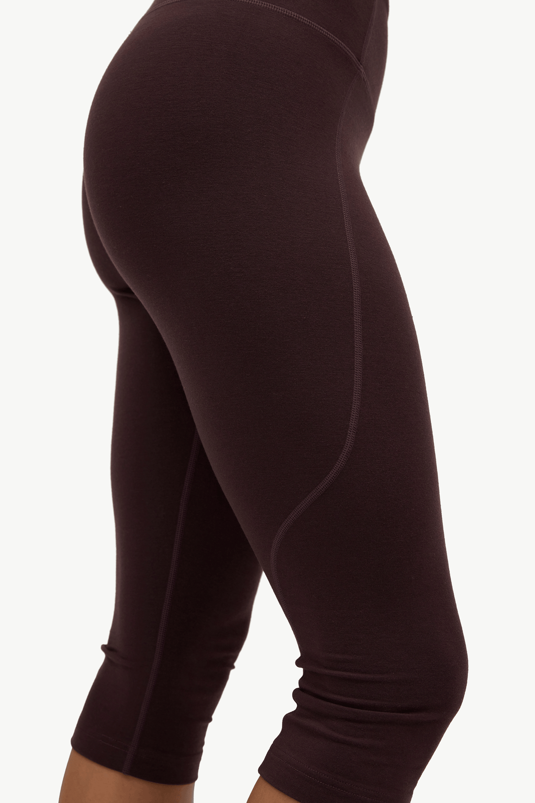 Close-up side view of a person wearing dark plum leggings against a plain light background.