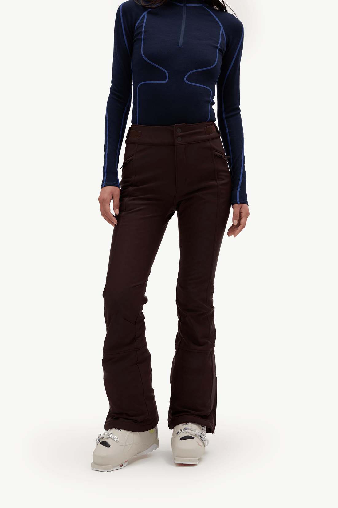 A model shown wearing a dark navy long-sleeve athletic top with bright blue contrast stitching, dark brown flared pants, a light blue headband, and white sneakers, set against a plain white studio background.