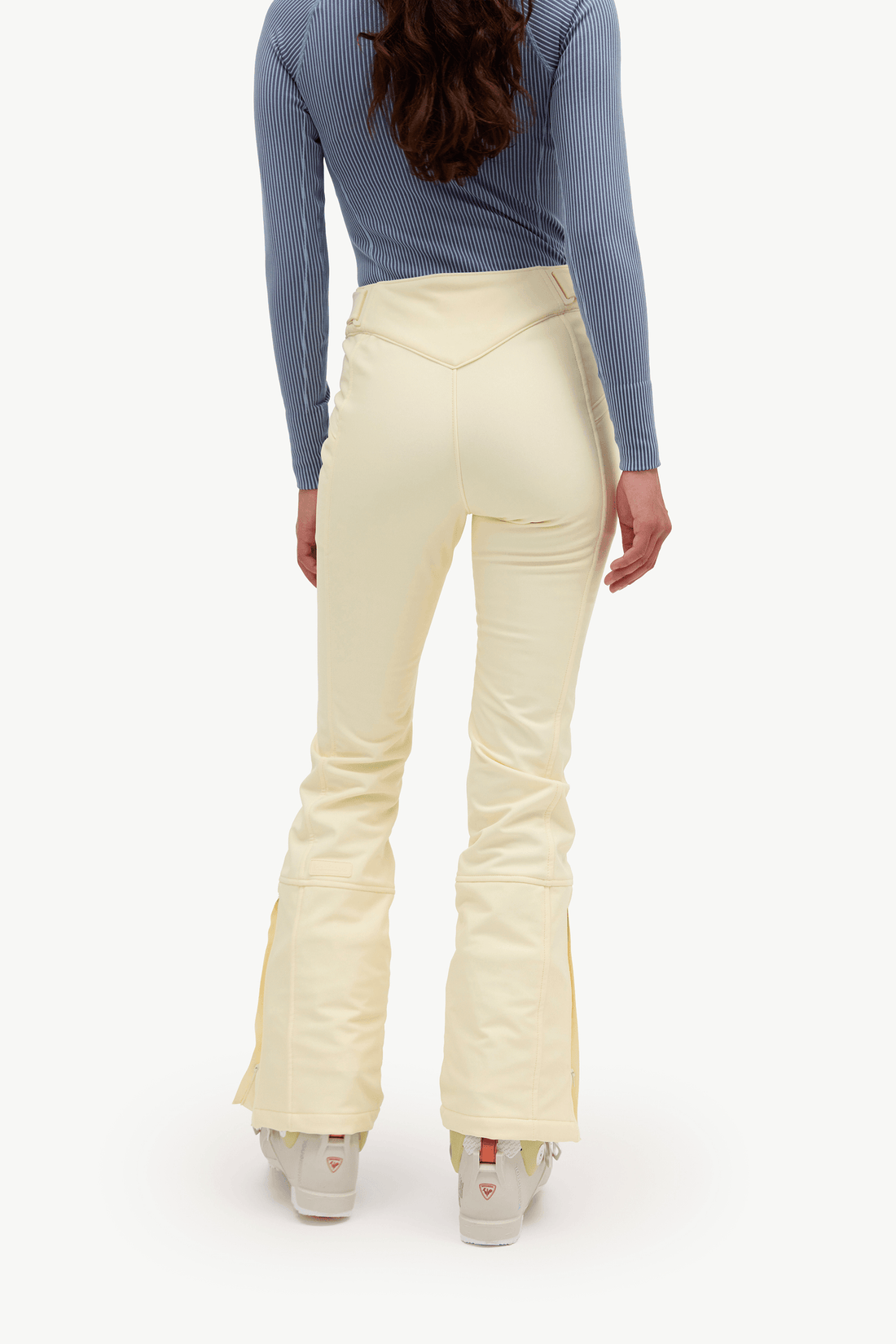 A model shown from the back wearing cream-colored flared pants, a blue long-sleeve top, and white sneakers against a plain white background.