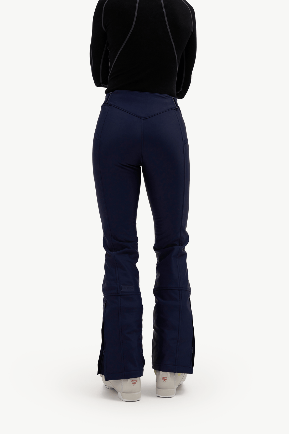 Rear view of a model wearing navy blue flared ski pants, a black long-sleeve top, and white sneakers against a plain white background.