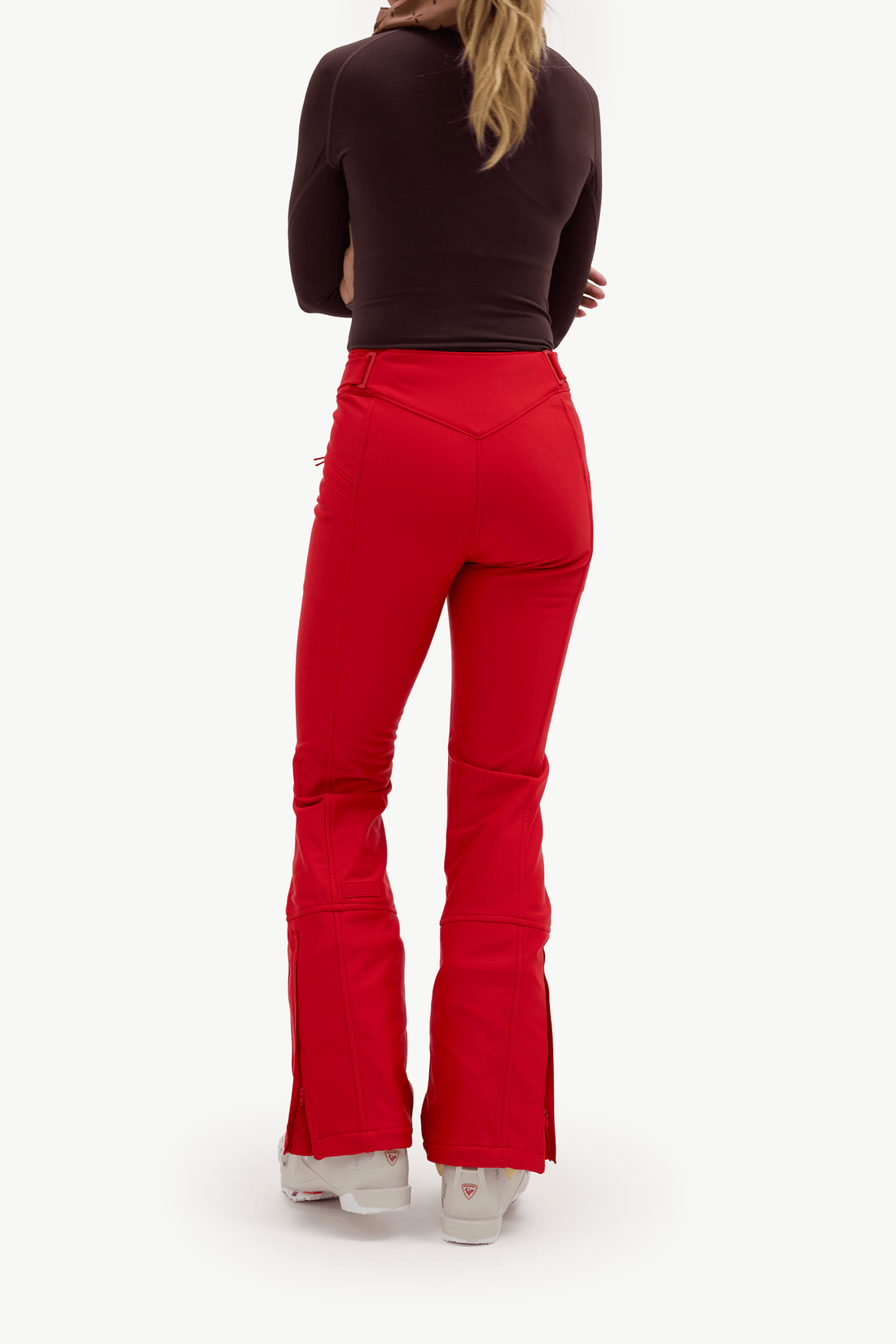 A model shown from the back wearing bright red flared pants, a dark brown long-sleeve top, and white sneakers against a plain white studio background.
