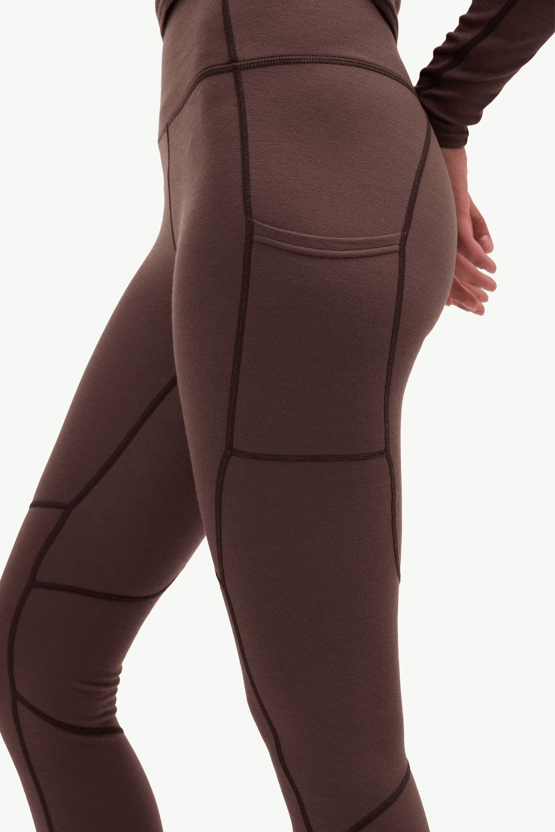 Close-up of a model wearing high-waisted athletic leggings in a dark brown color with contrasting black seam lines, shown from the side against a plain white background.