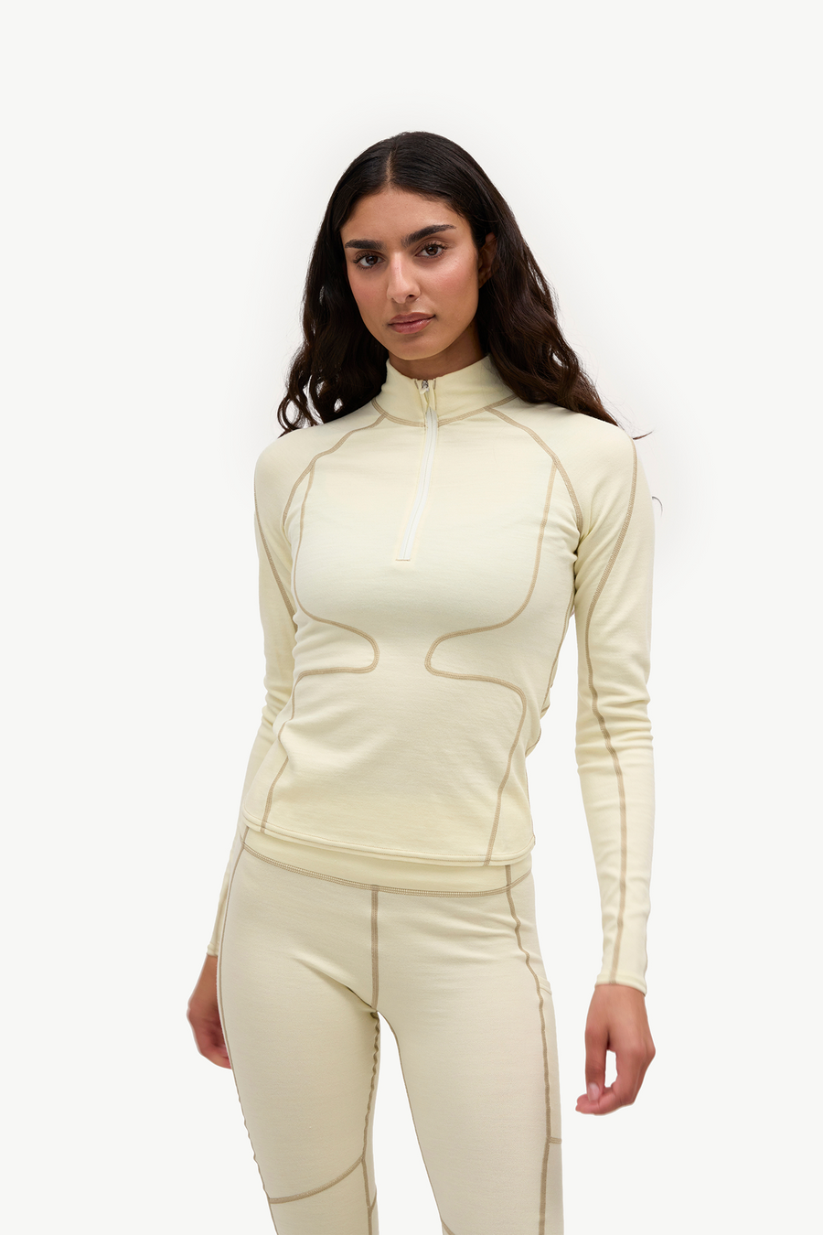A woman modeling a matching cream-colored athletic set consisting of a long-sleeve quarter-zip top and fitted leggings, shown against a plain white studio background.