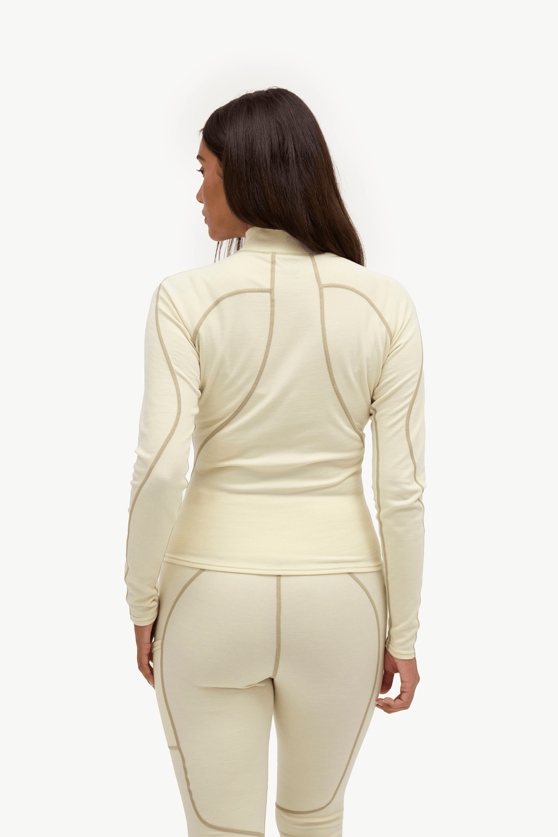 A woman shown from the back wearing a matching cream-colored long-sleeve athletic top and leggings set with contrasting tan seam detailing, against a plain white studio background.
