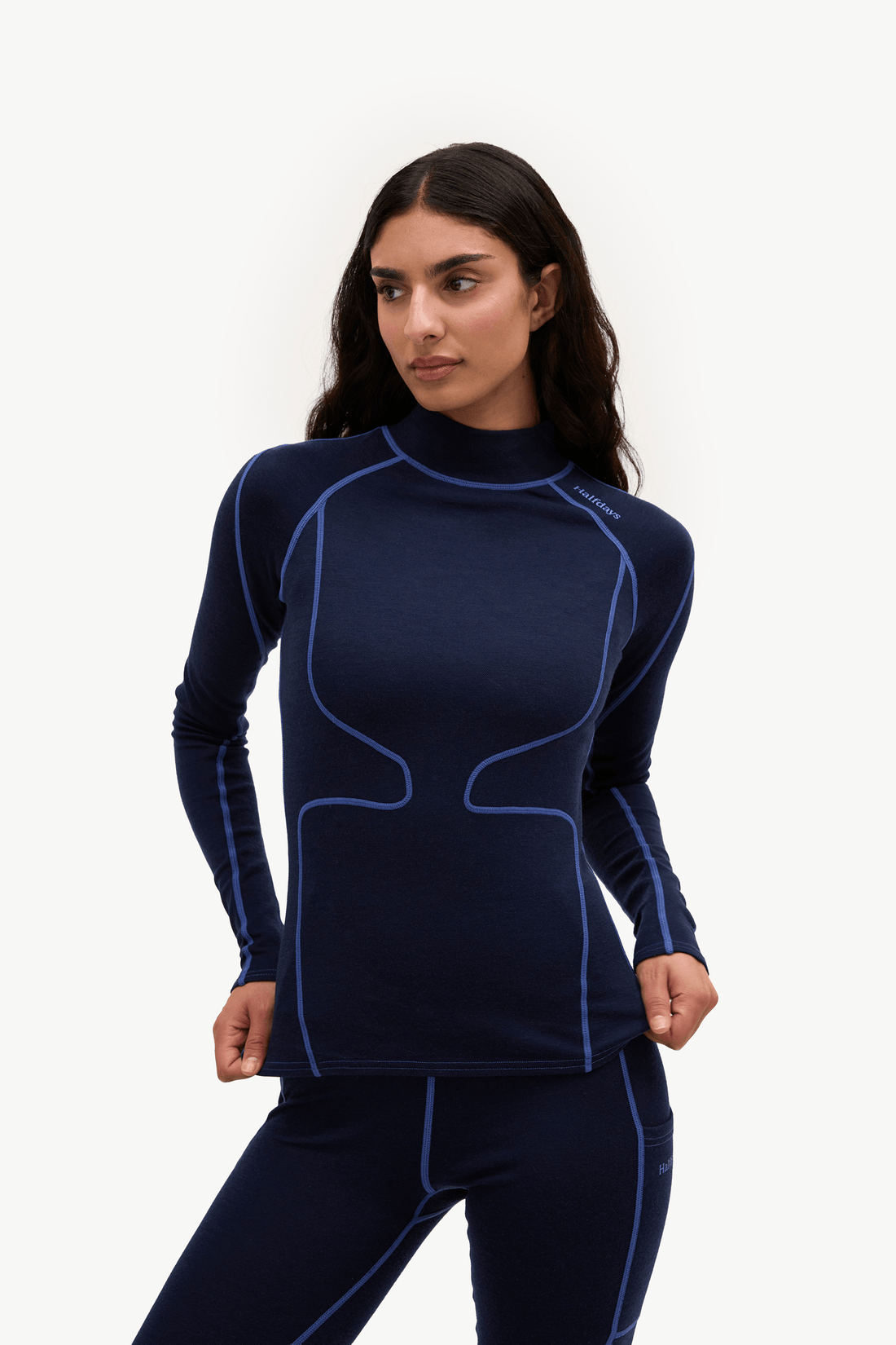 A woman modeling a dark navy blue long-sleeve athletic compression top with contrasting light blue piping, paired with matching leggings, against a plain white studio background.