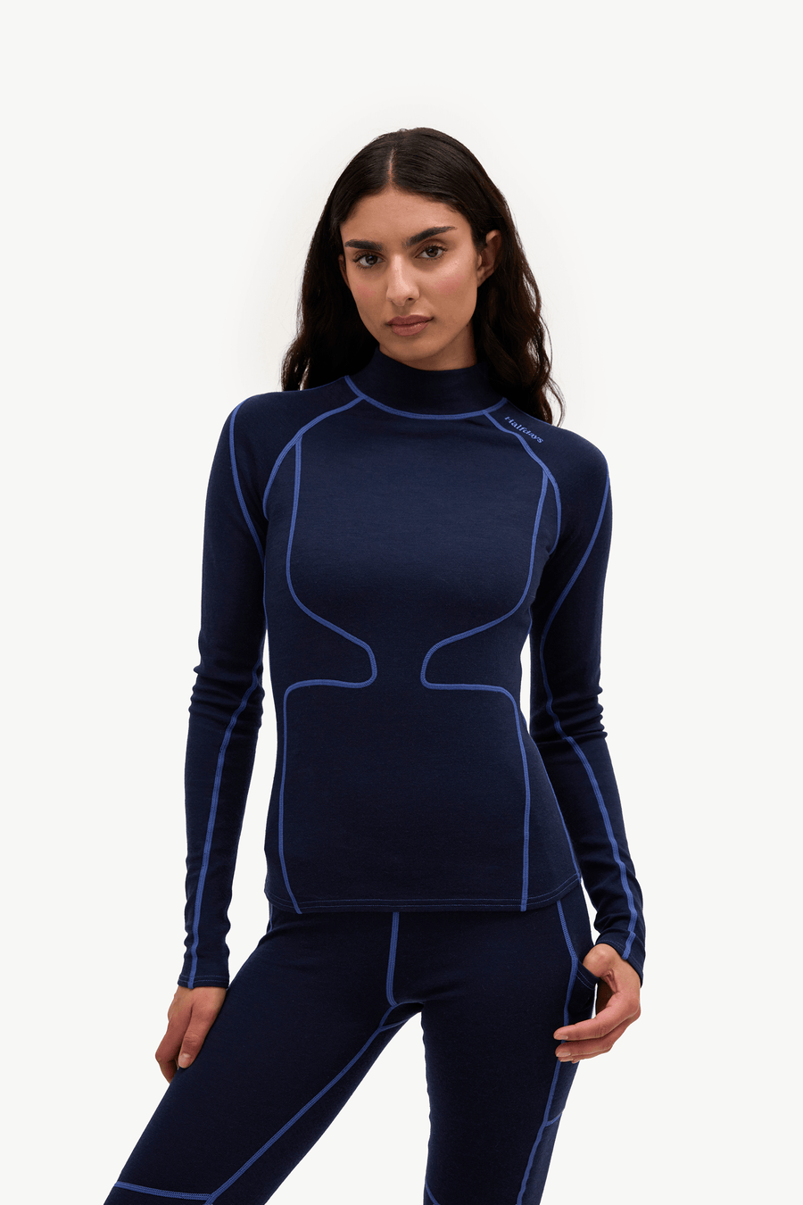 A woman modeling a dark navy blue long-sleeve athletic top and matching leggings with bright blue contrast stitching, set against a plain white studio background.