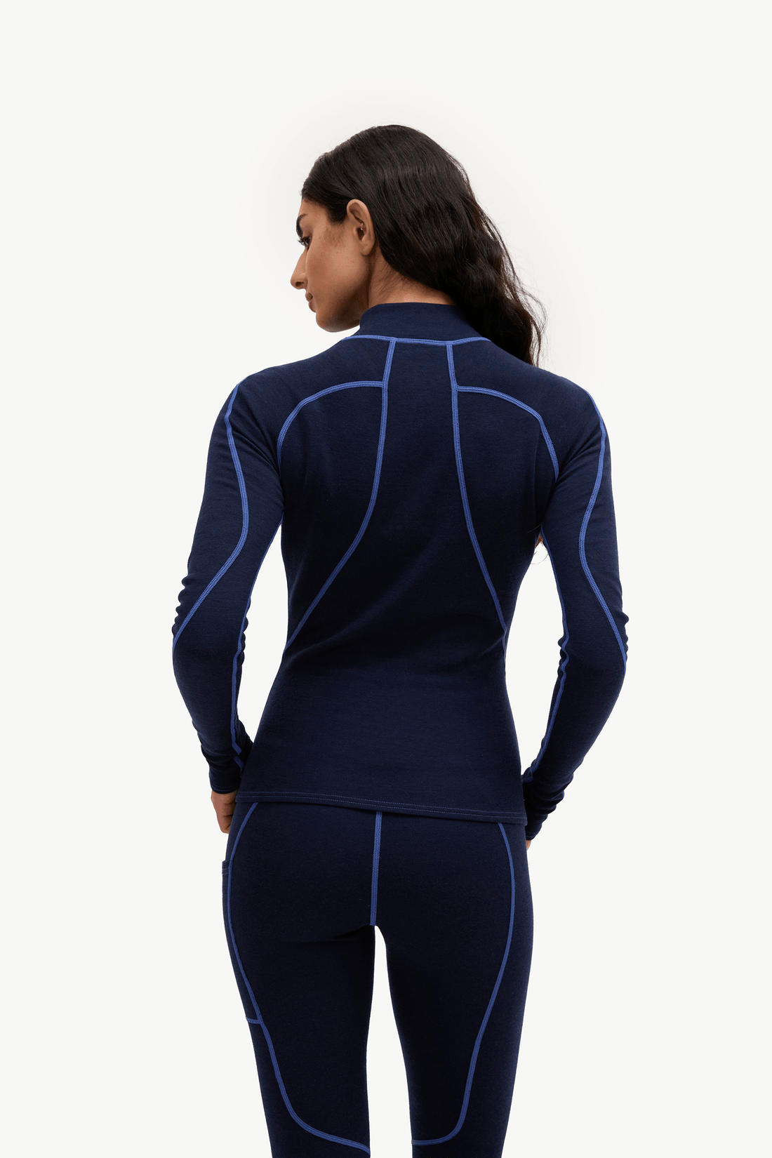 A woman shown from the back wearing a dark navy long-sleeve athletic top and matching leggings with bright blue contrast stitching, against a plain white studio background.