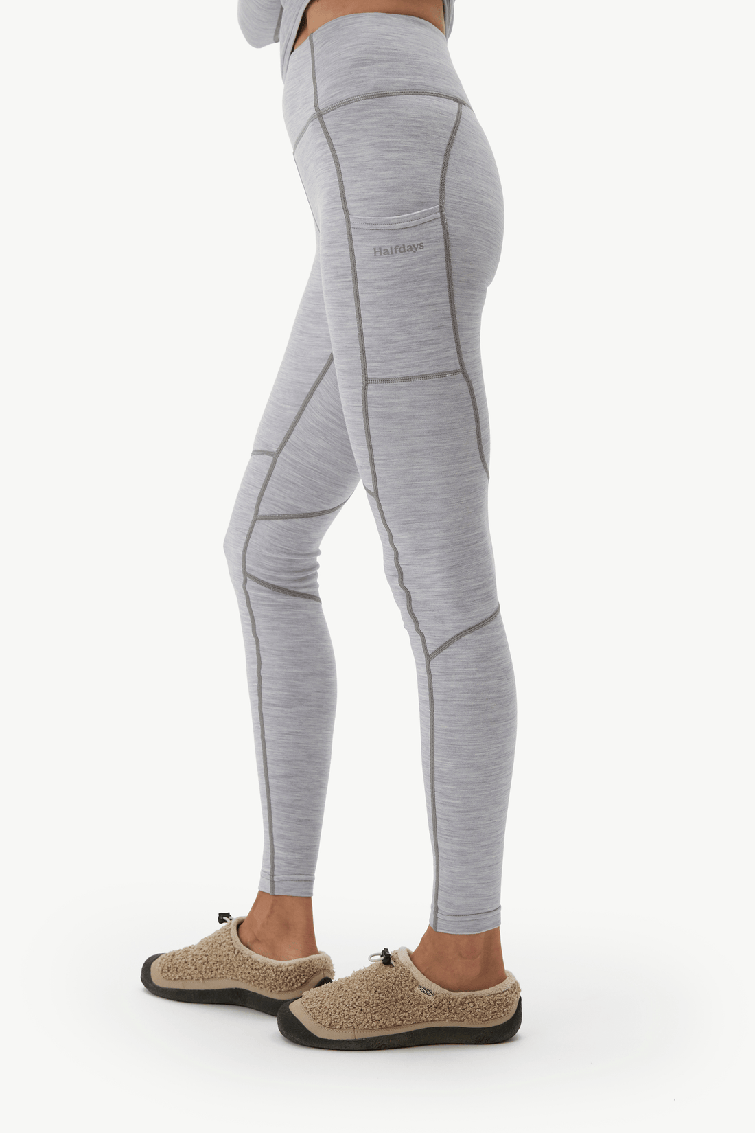 Light gray heathered athletic leggings with contrast stitching and a side pocket, shown on a model from the waist down wearing beige slip-on slippers against a white background.