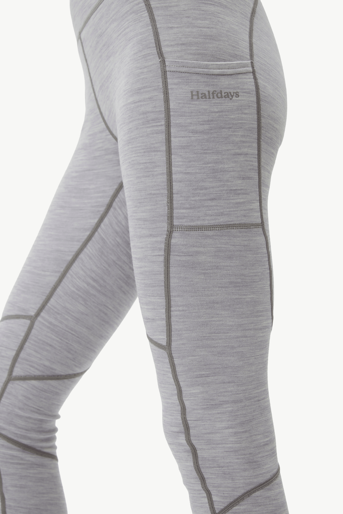 Close-up of a person wearing heather gray athletic leggings with dark gray seam lines and a small 'Halfdays' logo on the upper thigh, against a plain light background.
