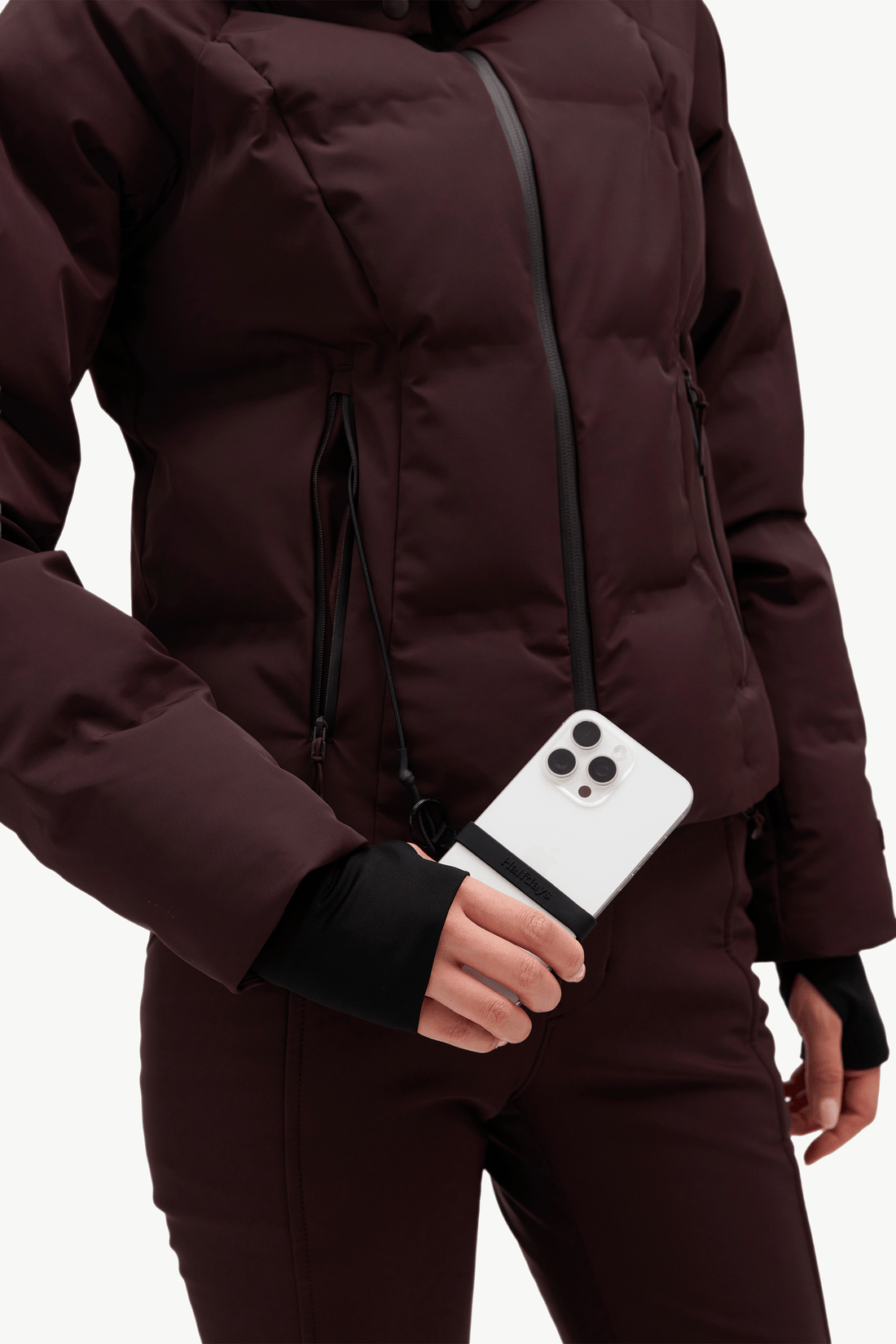A model wearing a dark burgundy hooded puffer jacket, matching dark pants, and holding a phone against a clean white background.