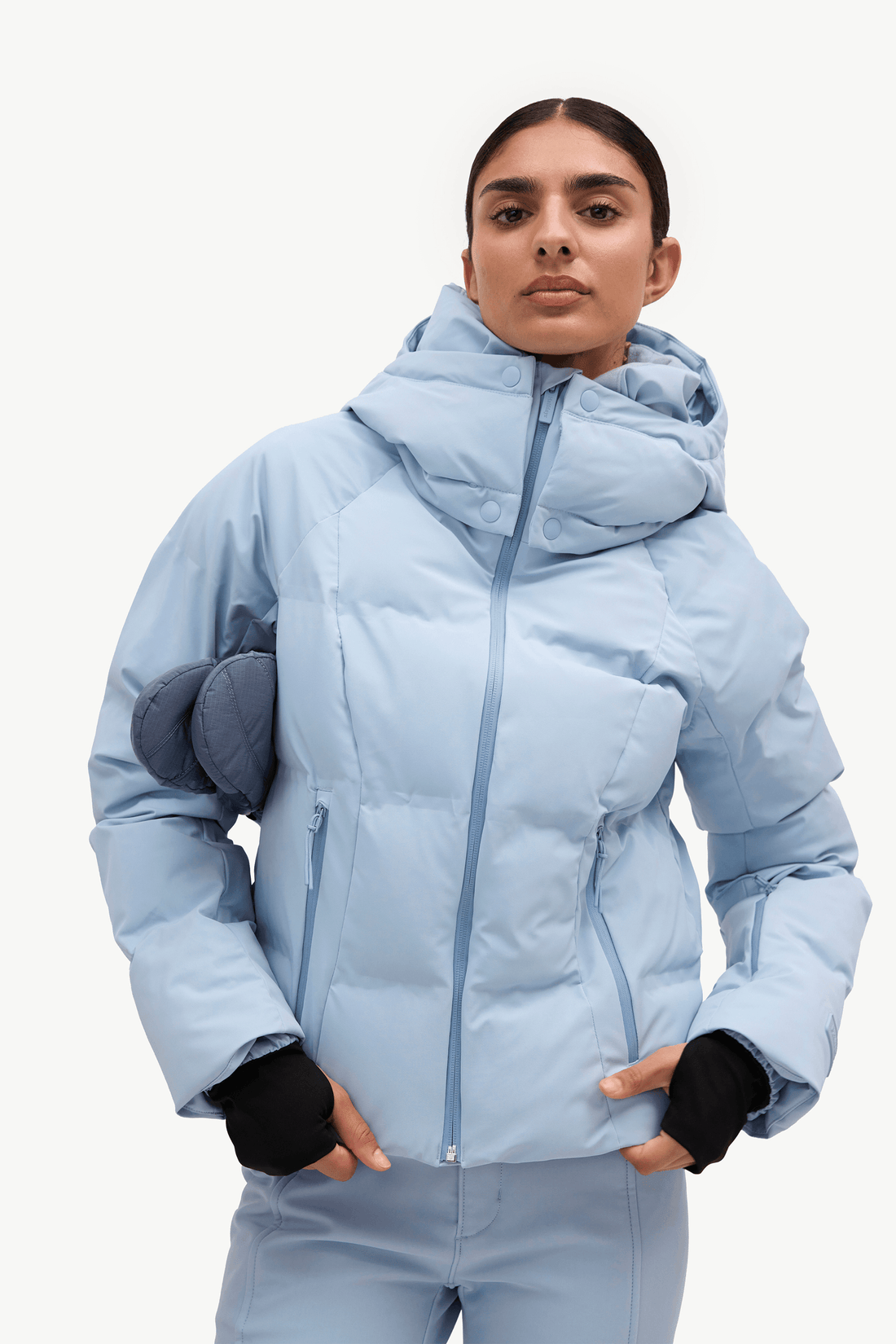 A woman in a light blue puffer jacket and matching flared ski pants against a plain white studio background.