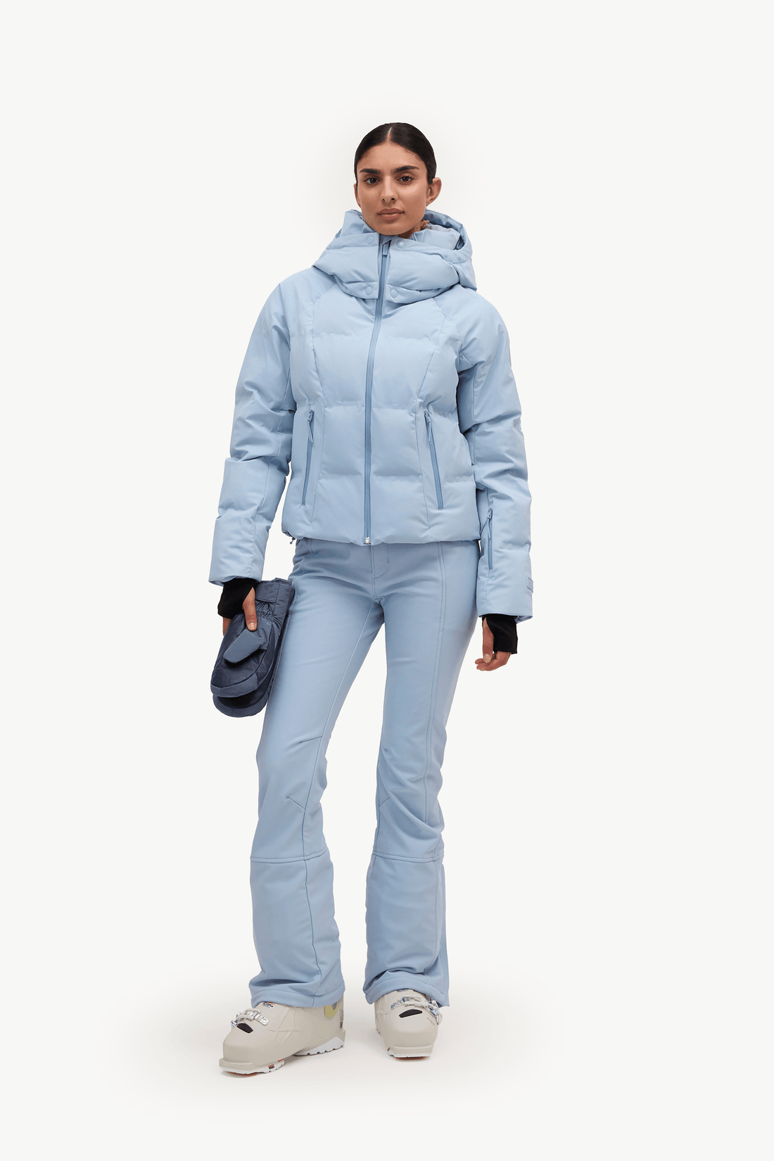 A woman in a light blue puffer jacket and matching flared ski pants, against a plain white studio background.