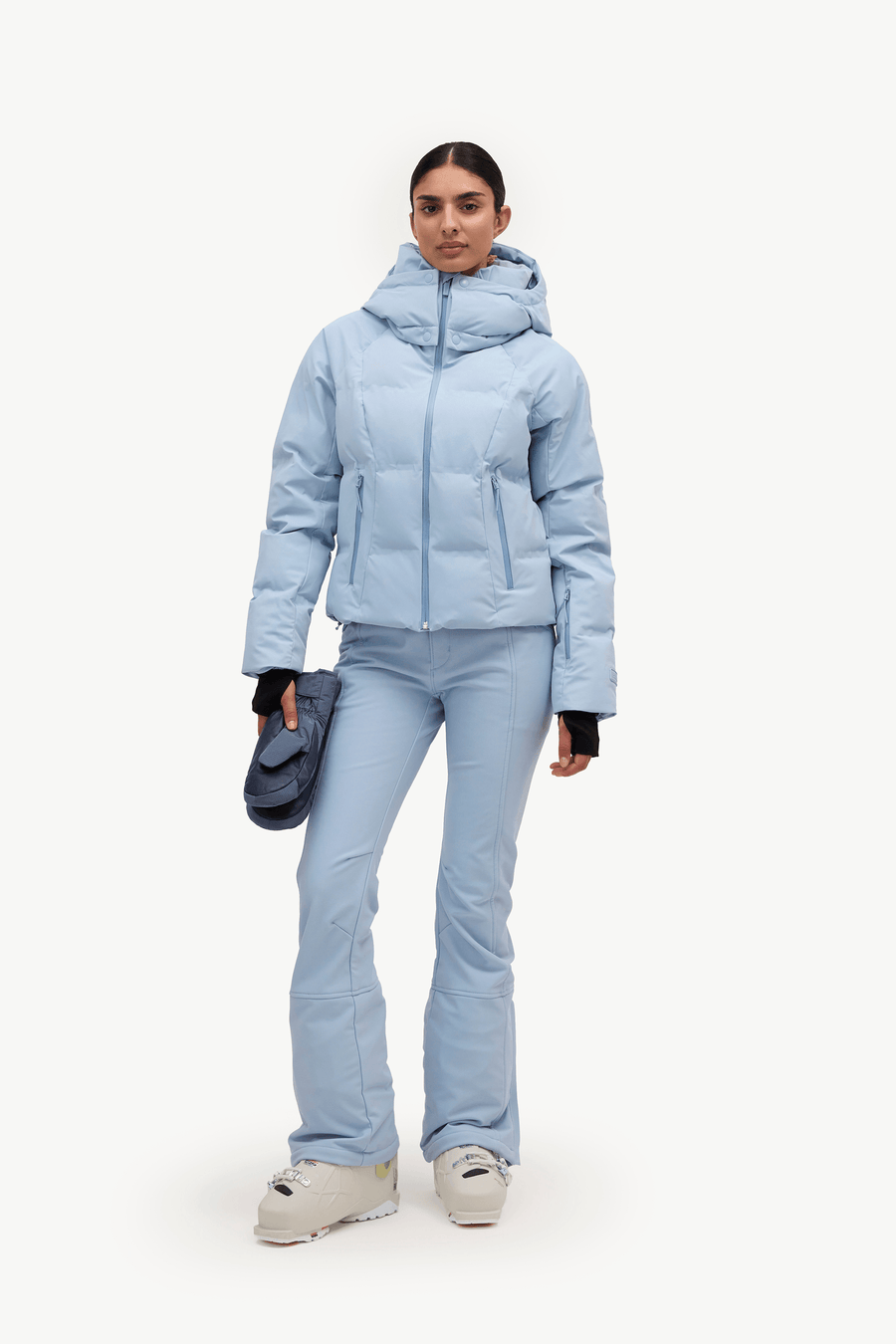A woman in a light blue puffer jacket and matching flared ski pants, against a plain white studio background.