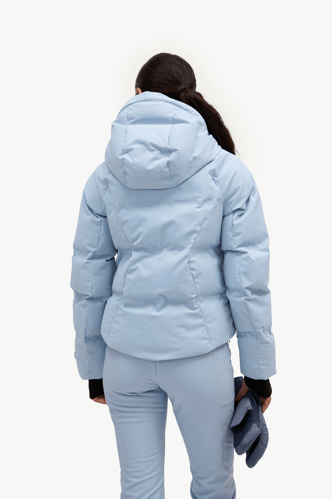 A woman in a light blue puffer jacket and matching flared ski pants, shown from the back against a plain white studio background.