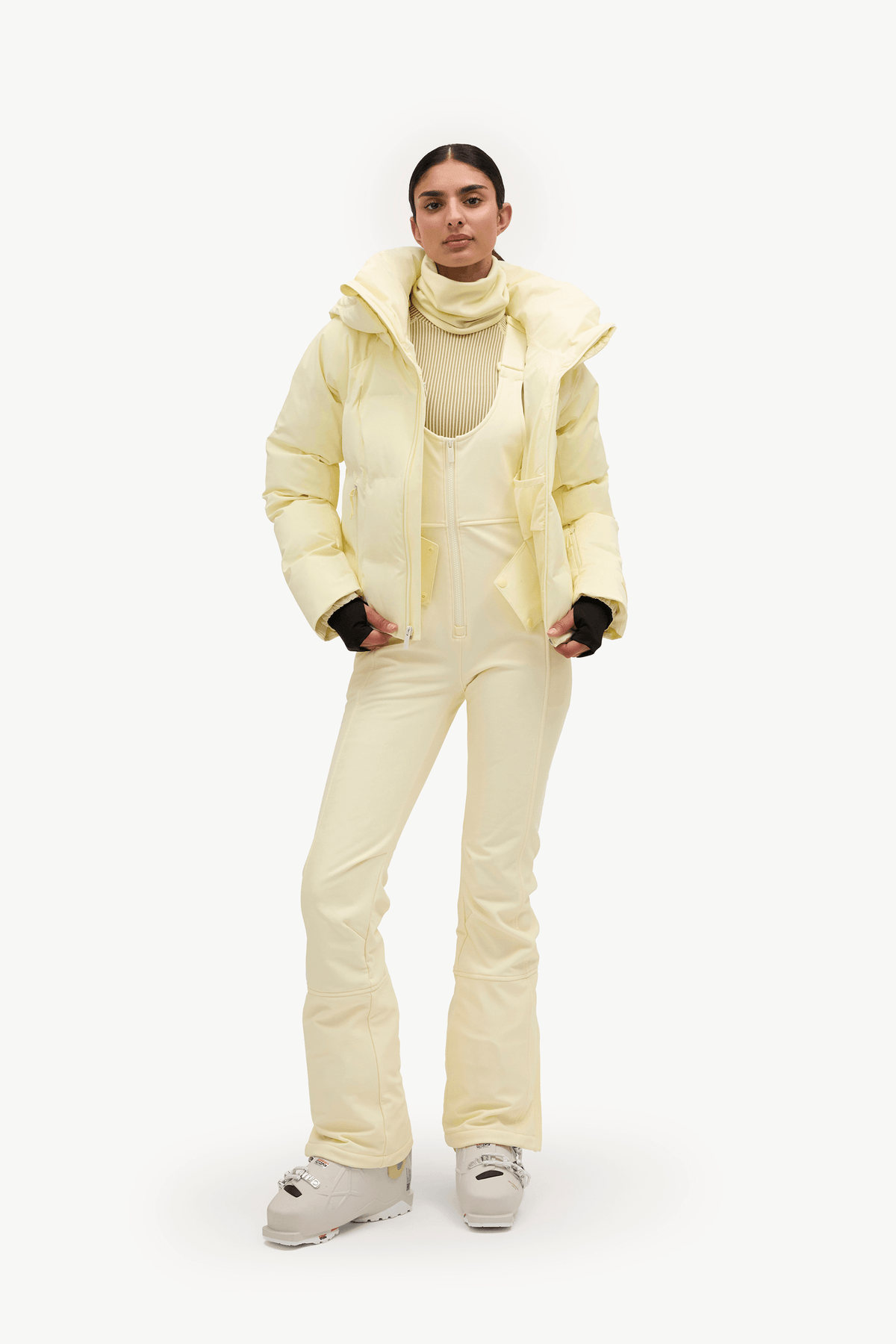 A woman wearing a pale pastel yellow puffer jacket and matching light pants against a clean white studio background.