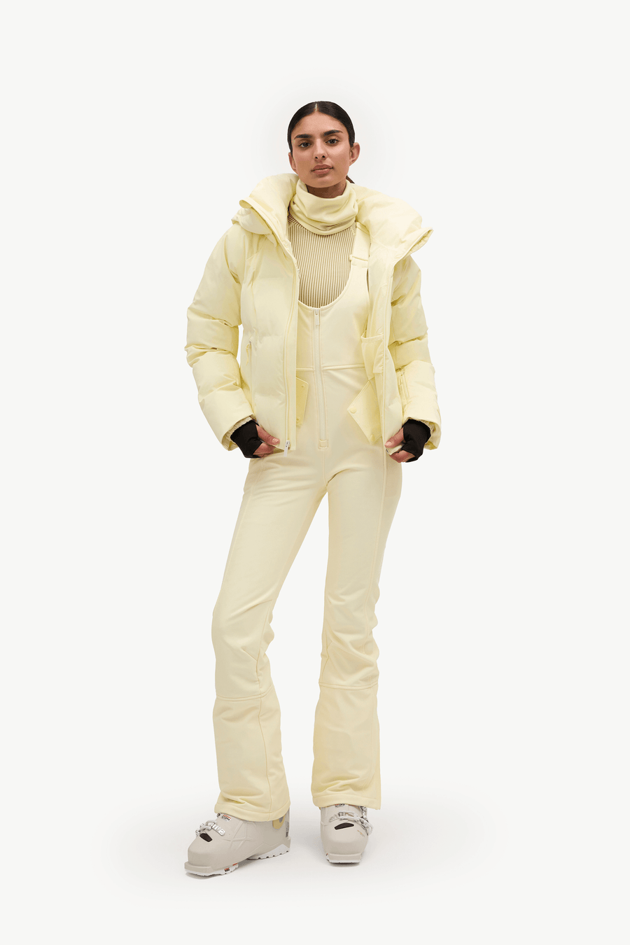 A woman wearing a pale pastel yellow puffer jacket and matching light pants against a clean white studio background.