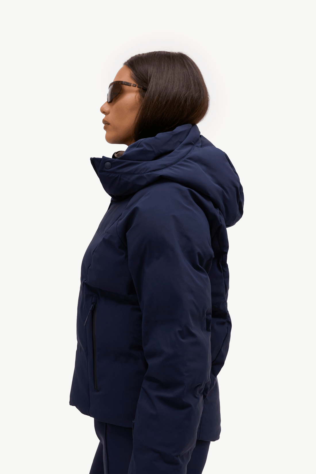 A model wearing a dark navy puffer jacket, matching navy pants, standing against a plain white studio background.
