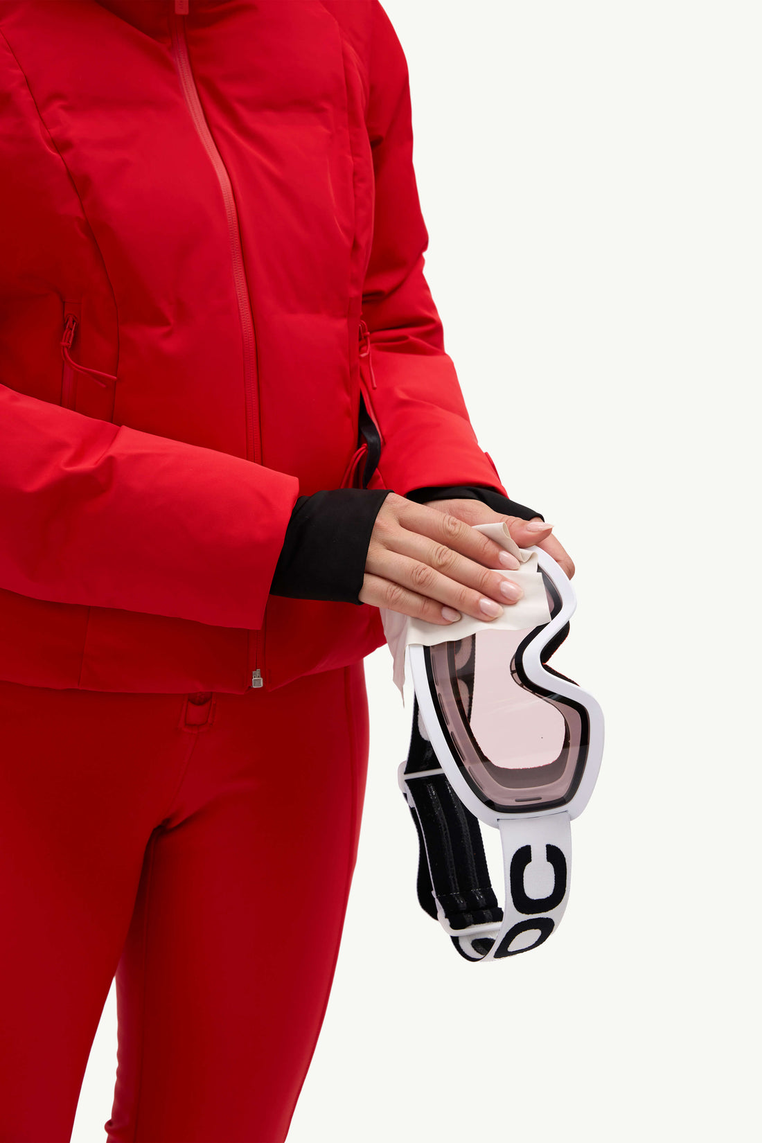 A model wearing a bright red ski jacket and matching red ski pants, holding goggles against a plain white studio background.