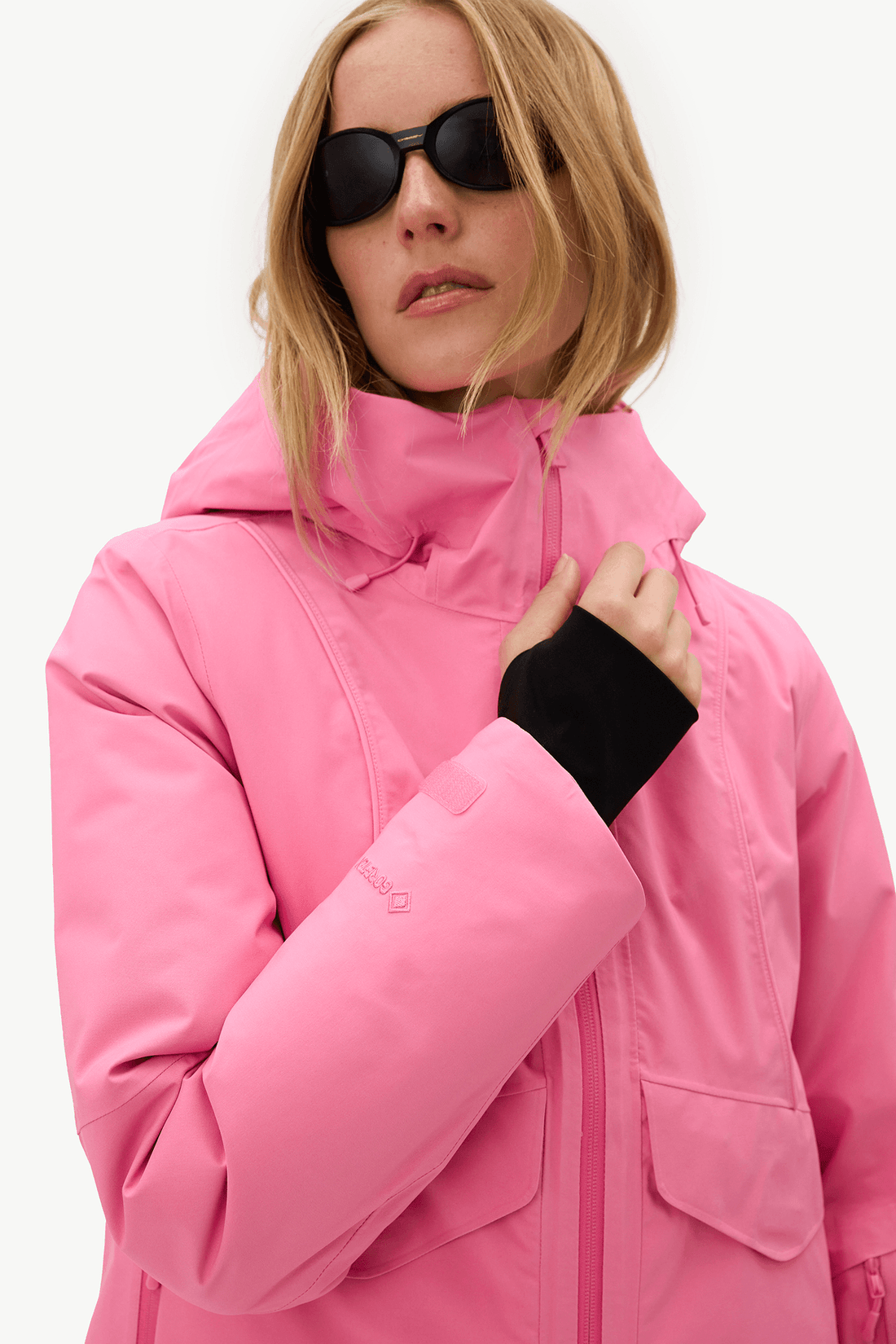 A woman wearing a bright pink ski jacket and black sunglasses, shown from the chest up against a clean white background.