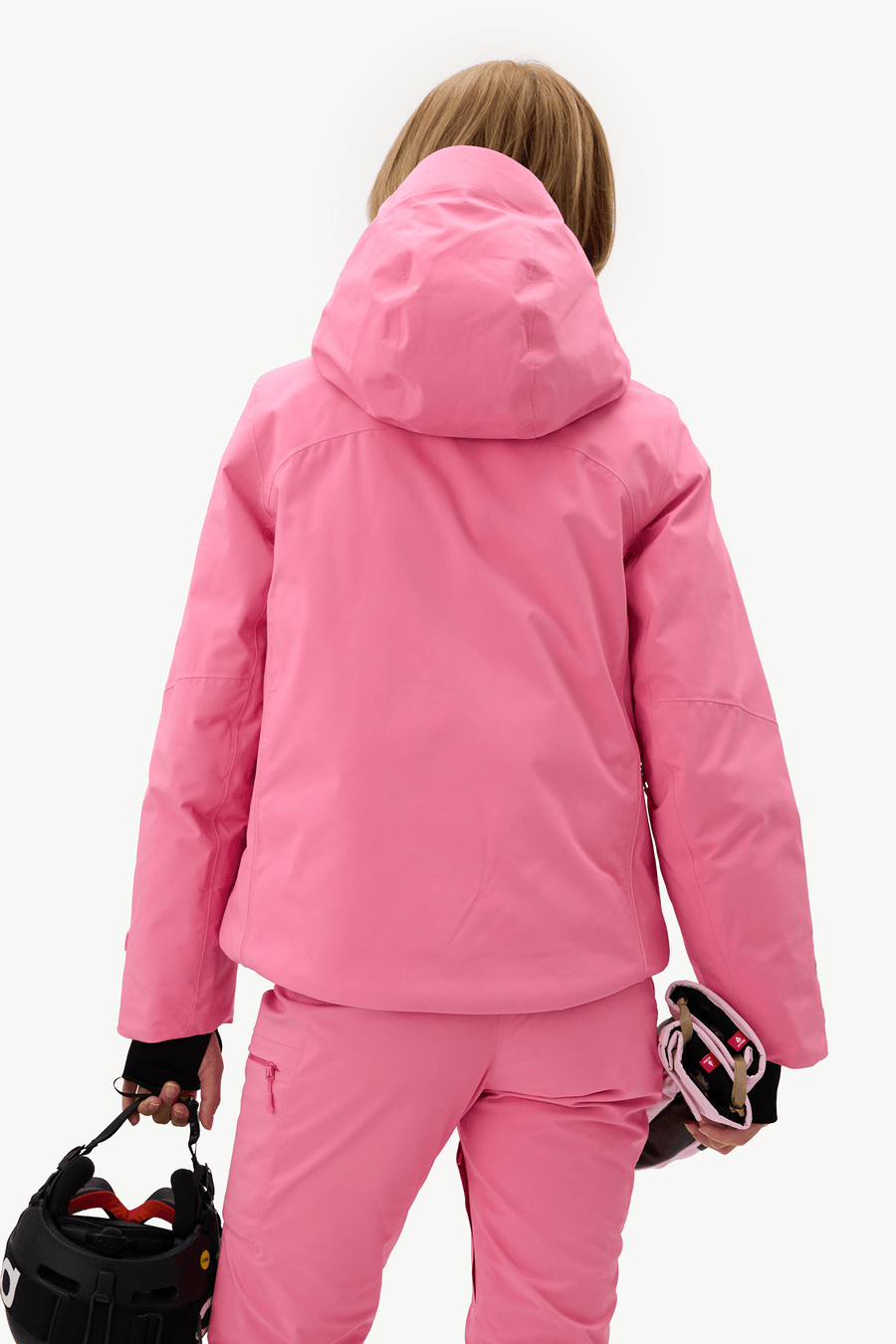 A person shown from the back wearing a bright pink hooded ski jacket and matching pink ski pants, holding a black helmet and goggles against a plain white studio background.