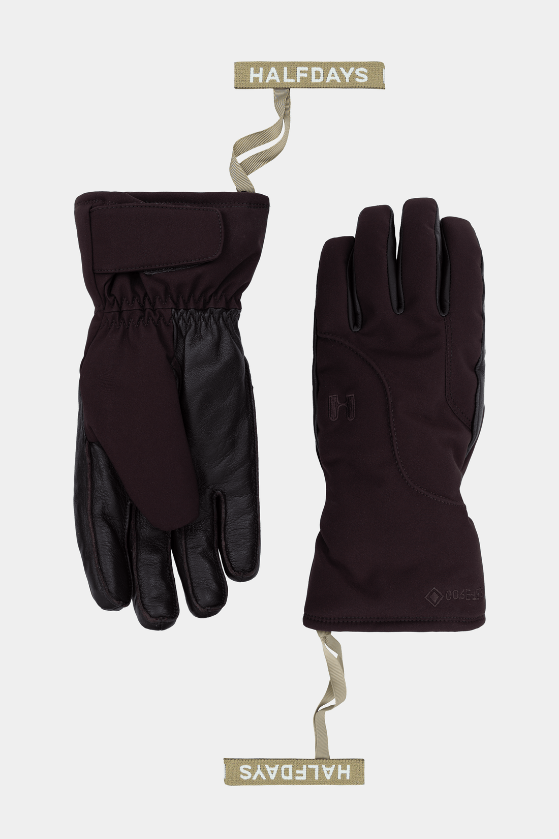 A pair of dark plum-purple and black winter gloves shown flat against a light gray background, with hanging tags labeled HALF DAYS.