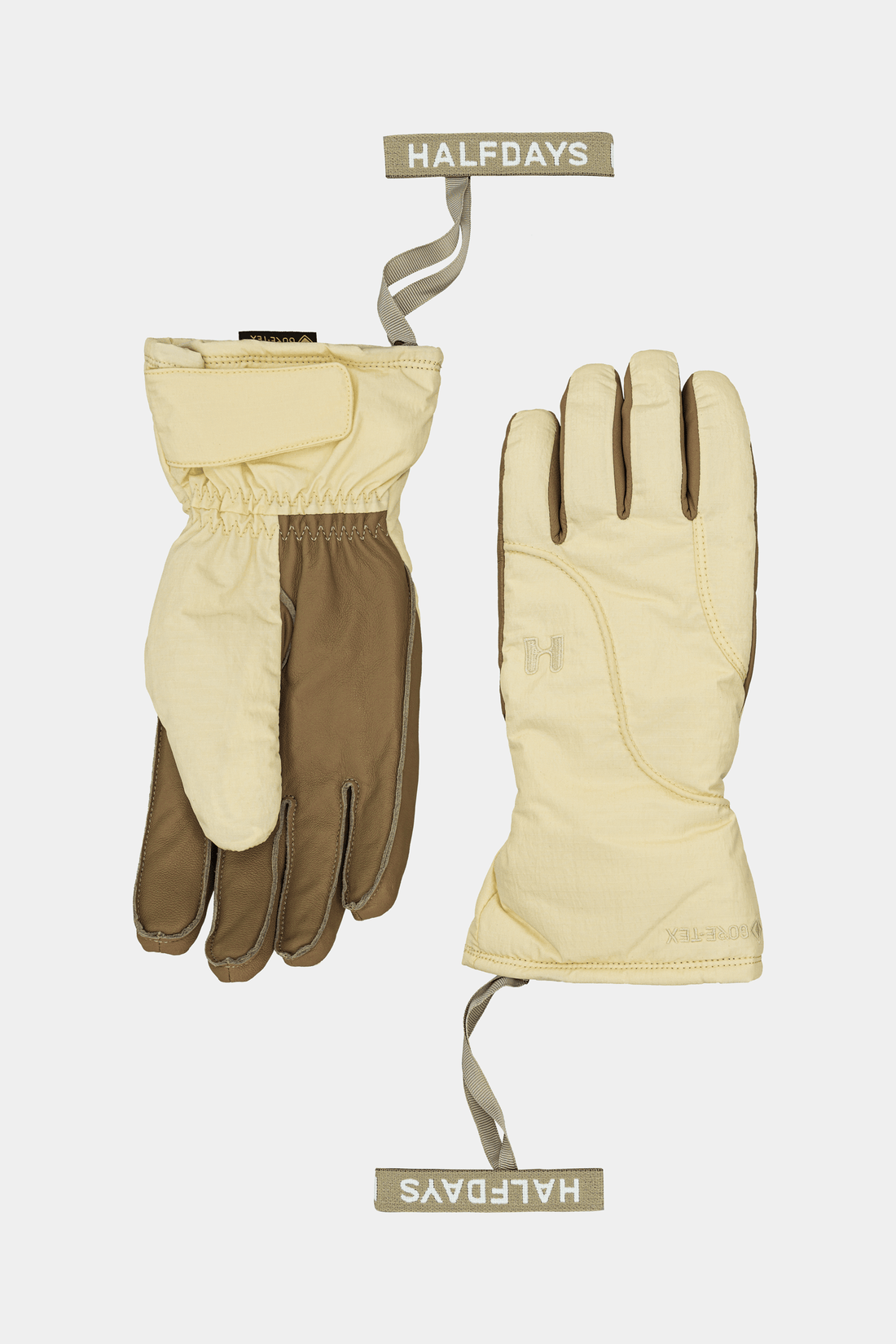 A pair of Halfdays winter gloves shown flat against a light gray background, with one glove displaying the back and the other showing the palm. The gloves are primarily a warm cream/beige color with brown reinforced sections on the fingers and wrist.