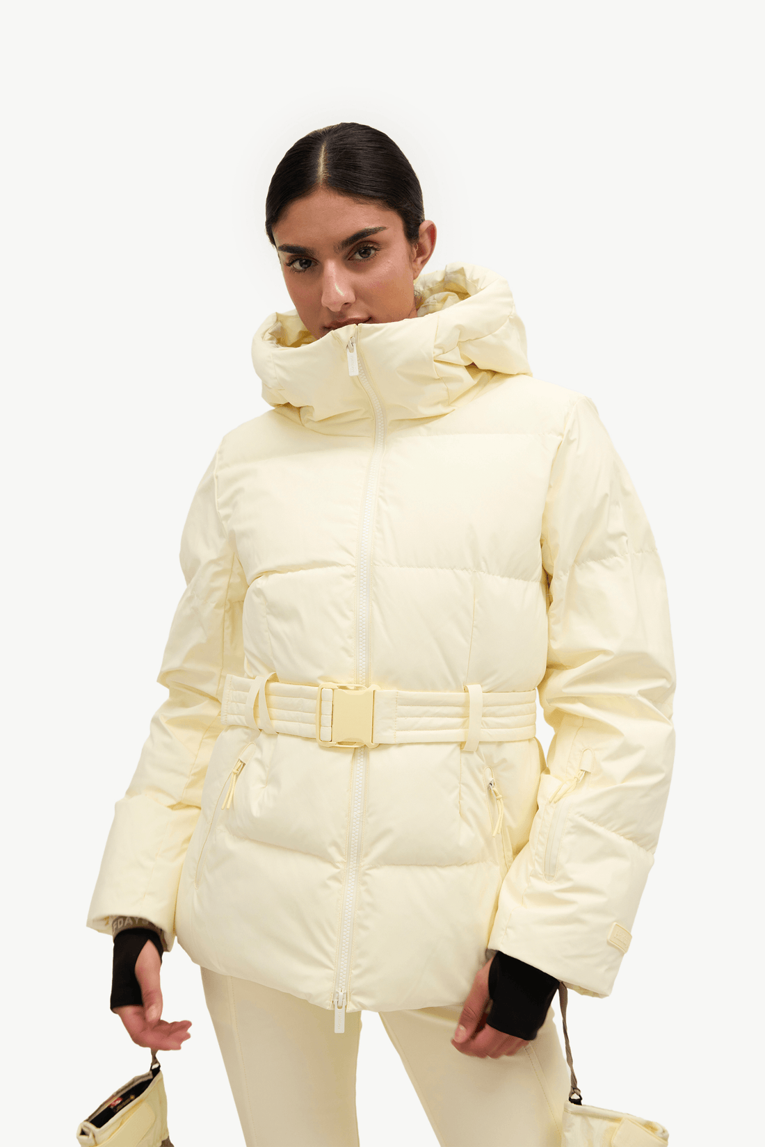 A model wearing a cream-colored puffer jacket with a matching belt and hood, paired with matching cream pants, against a plain white background.