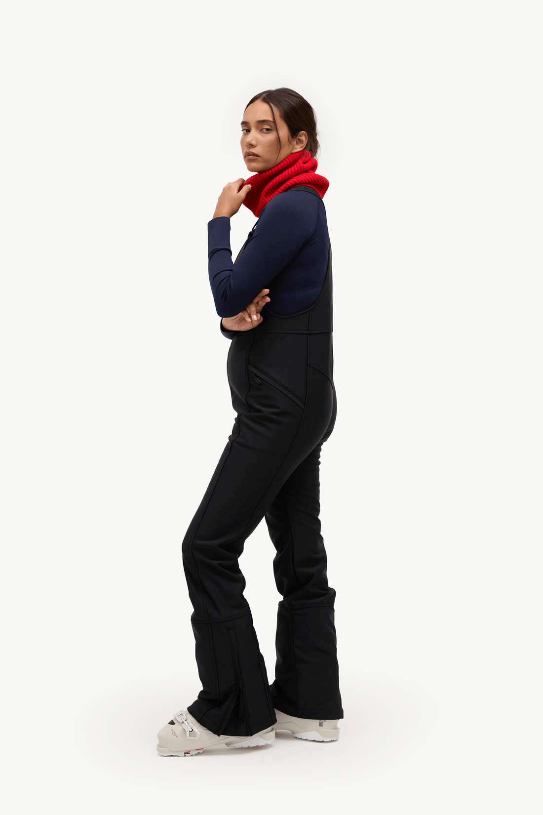 A woman modeling a pair of black flared pants with a navy blue long-sleeve top and a bright red scarf, standing against a solid white studio background.